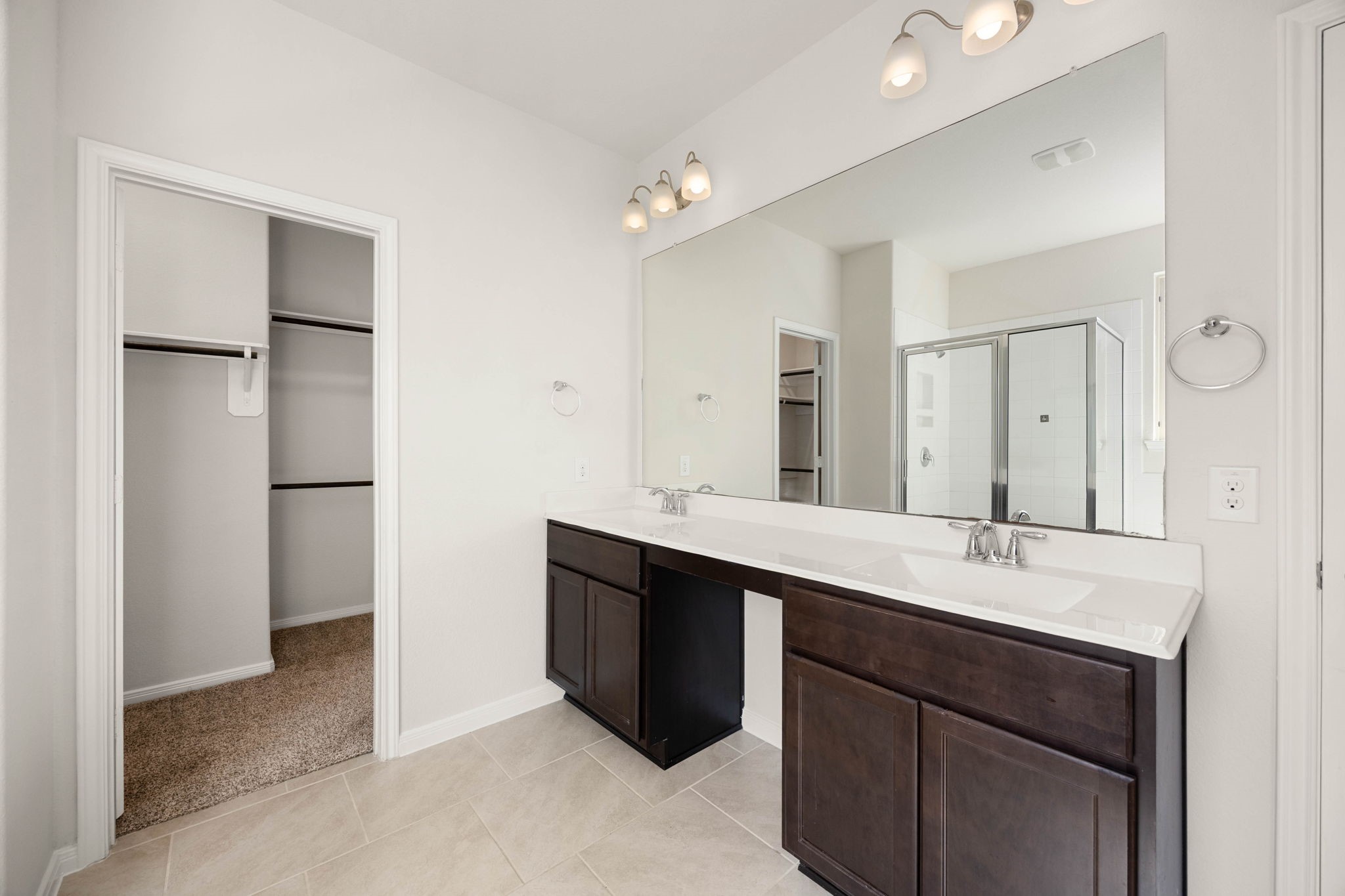 Luxurious primary bathroom retreat featuring an expansive double vanity, rich espresso cabinetry, and seamless access to a spacious walk-in closet.