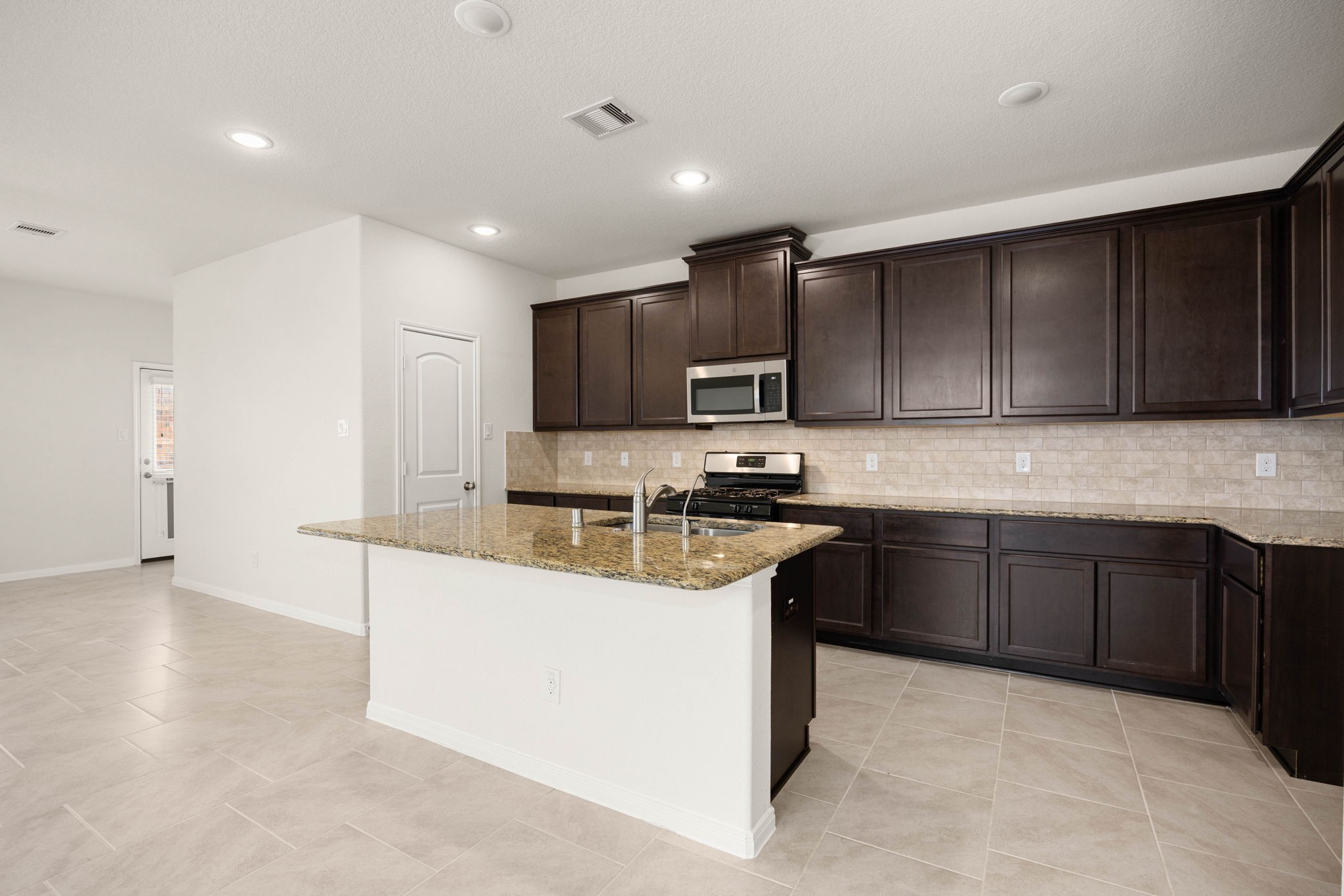 A chef-inspired kitchen designed for gathering, featuring rich cabinetry, granite countertops, stainless steel appliances, a spacious pantry, and an oversized island with bar seating. The open-concept layout flows effortlessly into the living and dining areas, making entertaining and everyday living both stylish and functional.