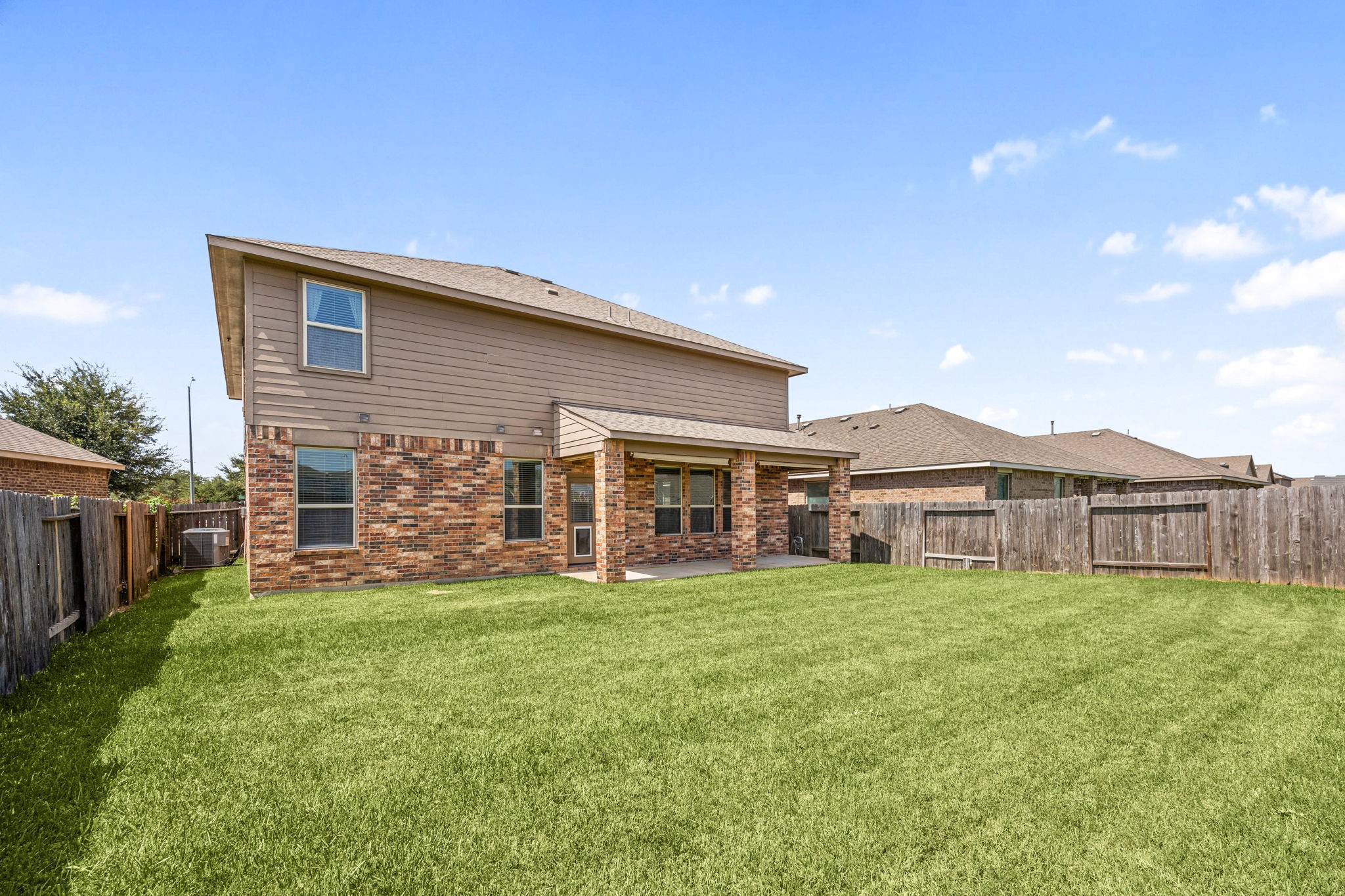 Impressive two-story rear exterior featuring a partial brick facade, a spacious covered porch, and a vast, fully fenced backyard.