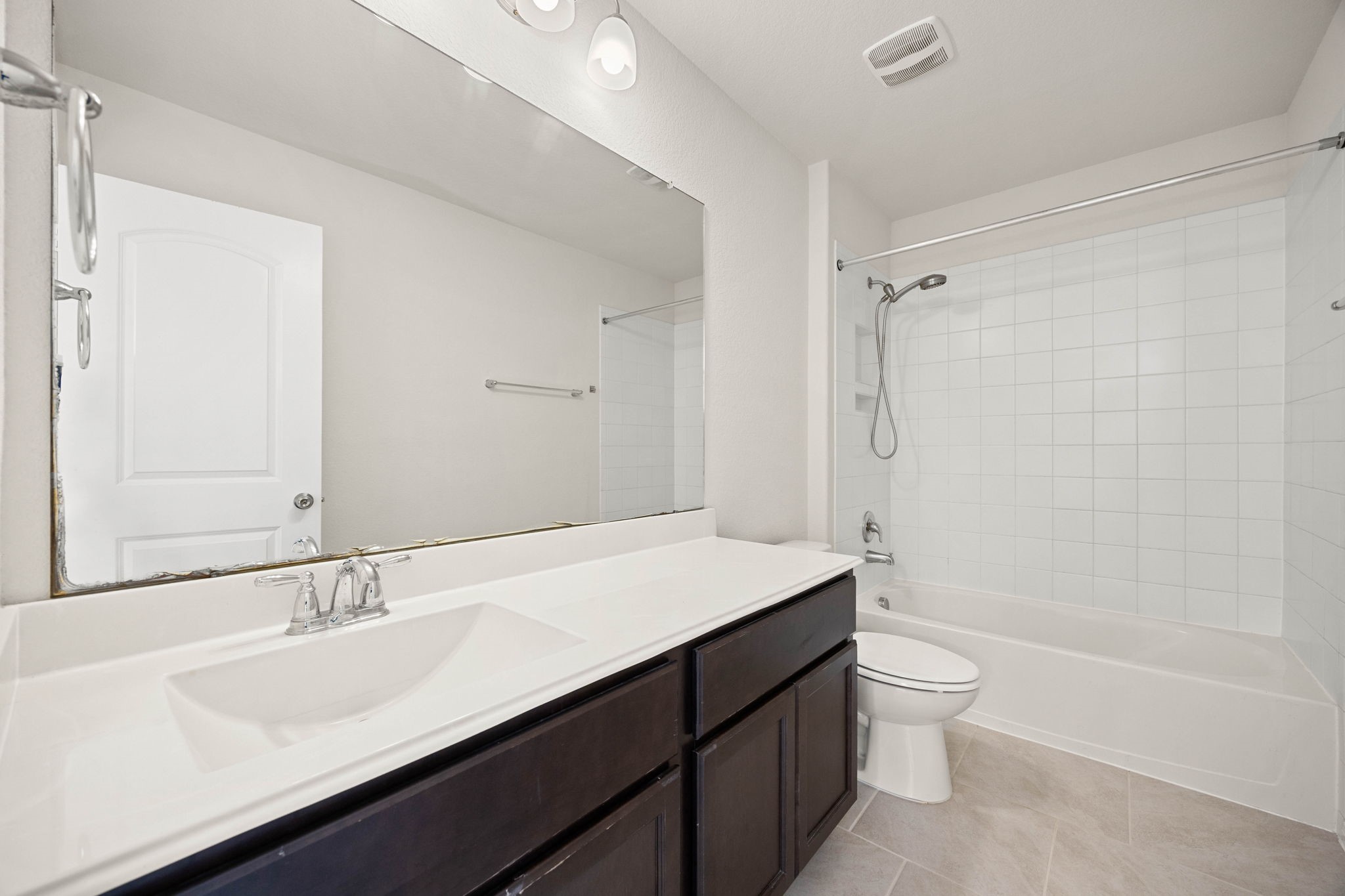 Crisp and modern secondary bathroom featuring a spacious vanity with integrated storage, an oversized mirror, and a classic tub-to-ceiling tile shower surround.