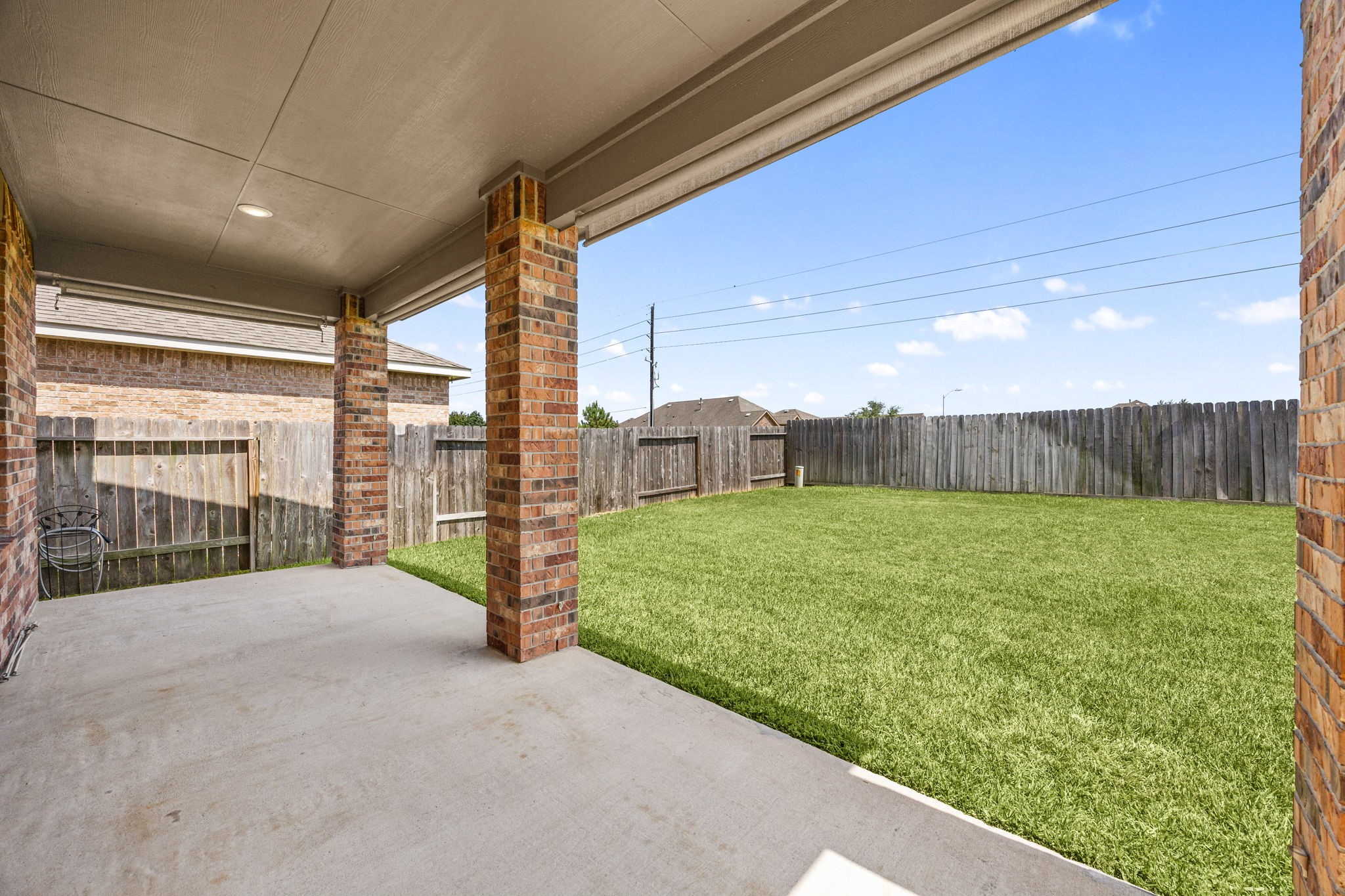Expansive backyard retreat featuring a massive covered concrete patio, classic brick support pillars, and a fully fenced green lawn
