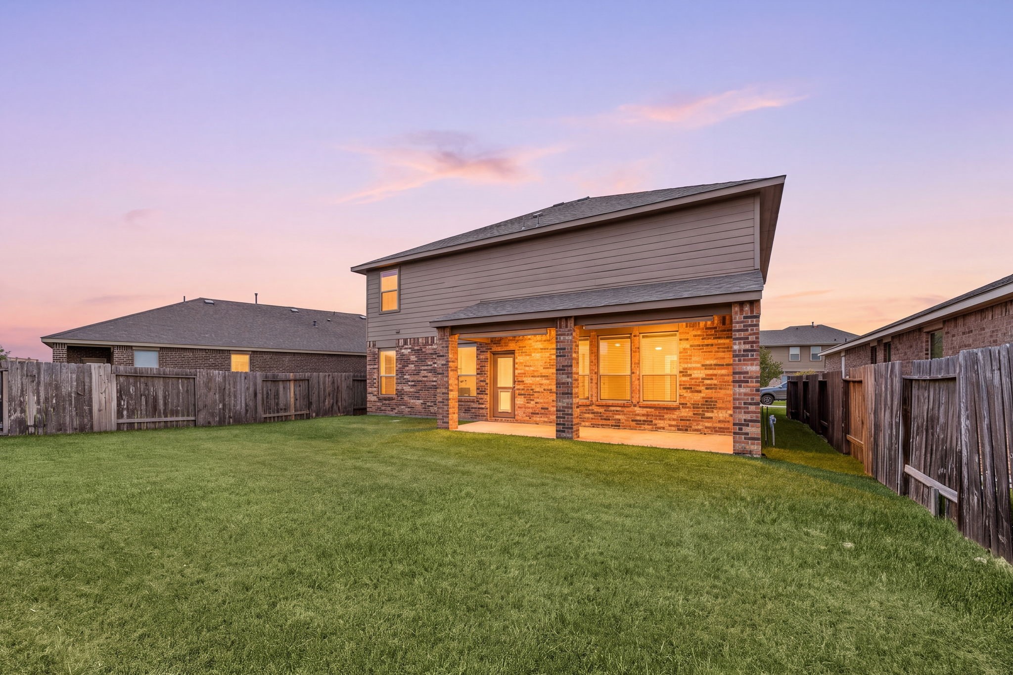 Stunning twilight view of the two-story rear exterior highlighting a warm, glowingly lit covered patio and an expansive grassy backyard.