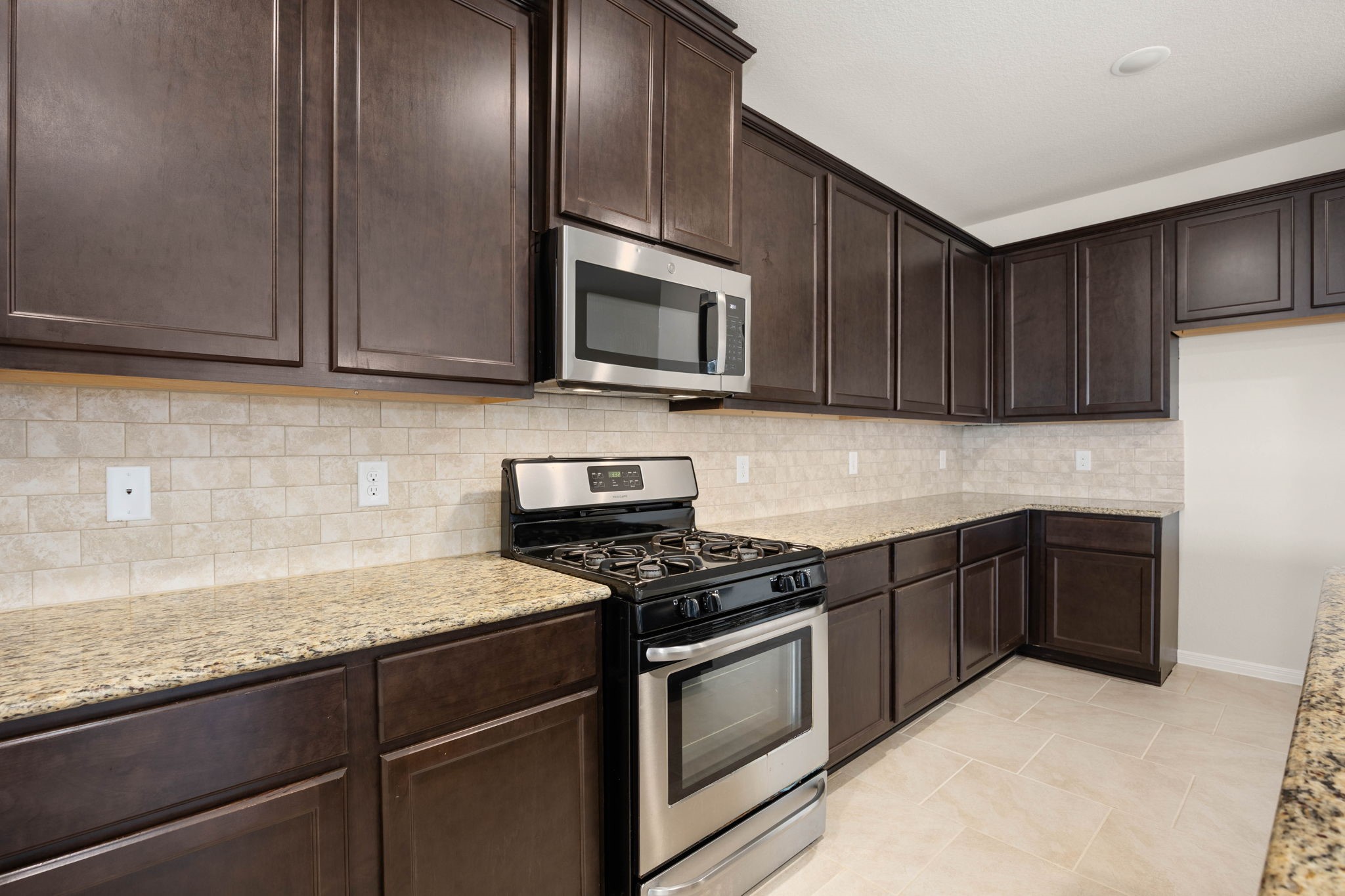 Warm and inviting culinary haven featuring expansive earth-toned granite countertops, continuous premium espresso cabinetry, and sleek integrated stainless steel appliances.