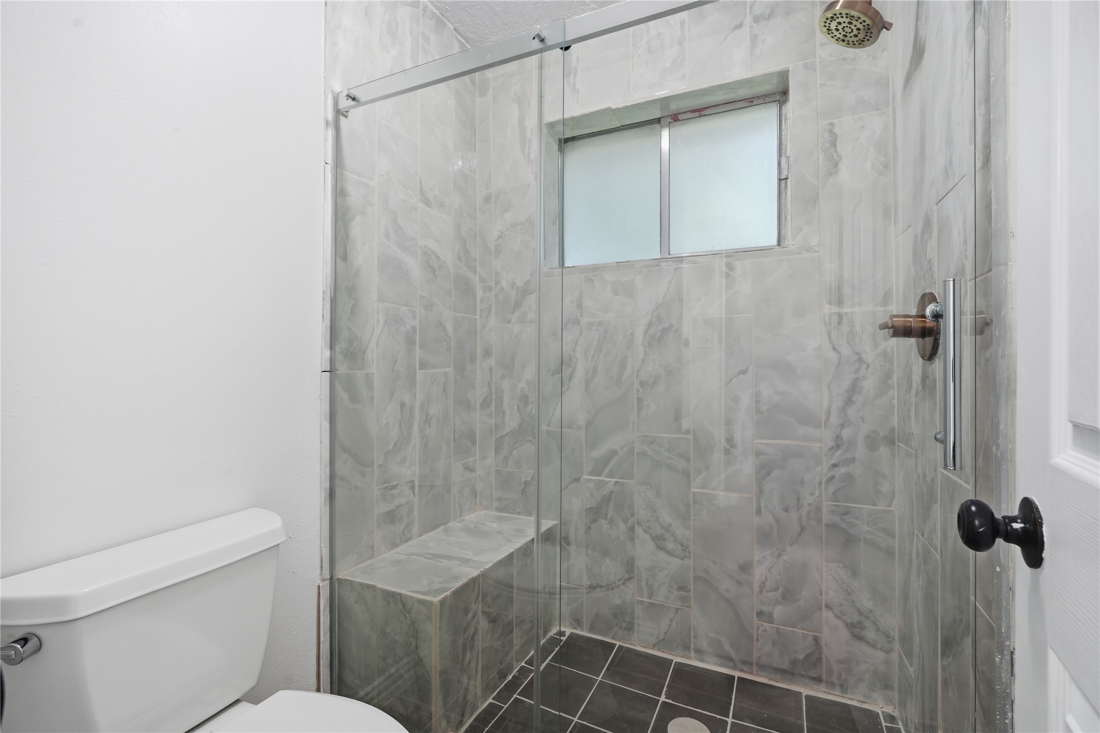Updated primary bath with a beautifully tiled walk-in shower featuring a built-in bench, glass enclosure, and modern fixtures.