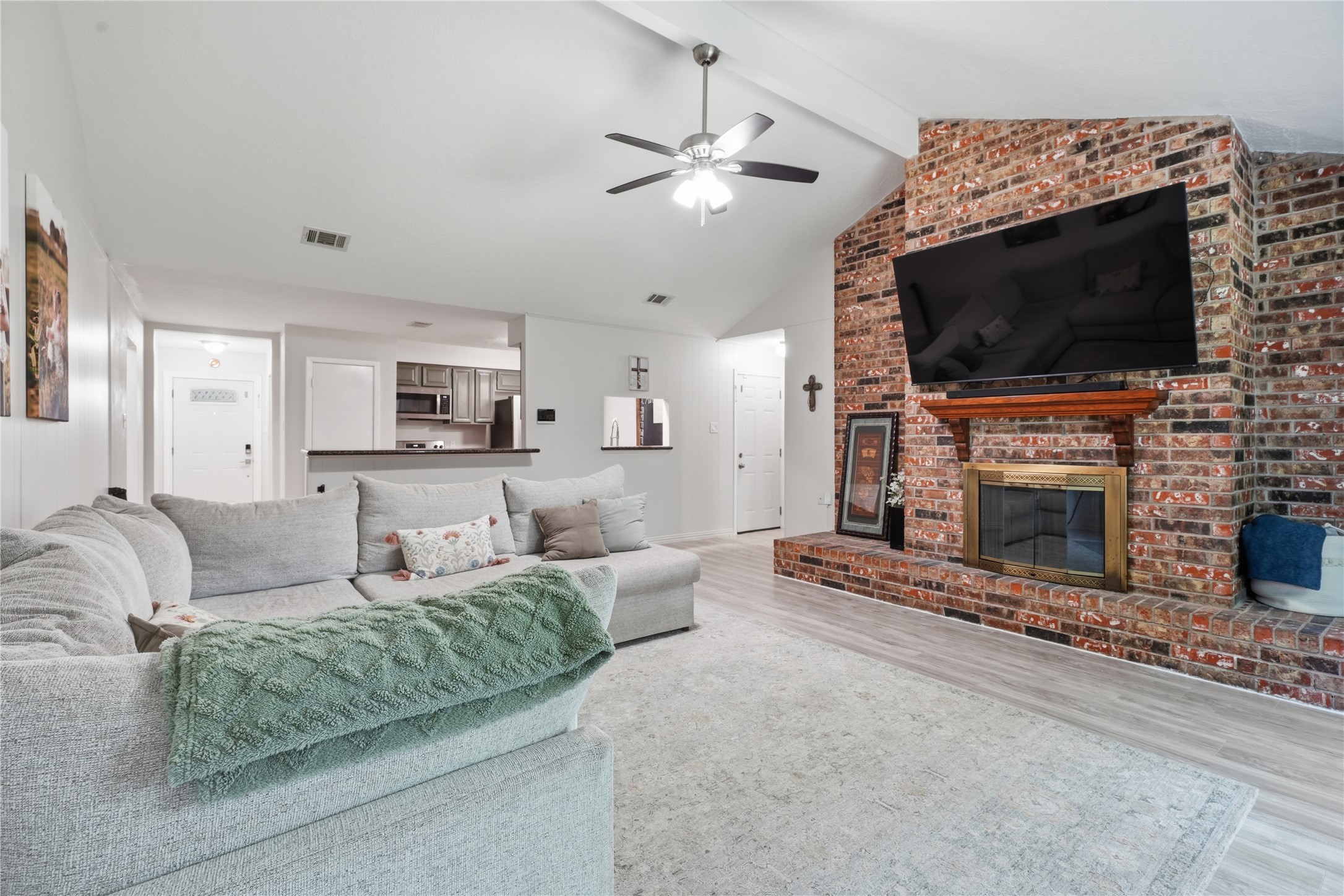 Inviting living area highlighted by a floor-to-ceiling brick fireplace, vaulted ceiling, and open sightlines to the kitchen and entryway.