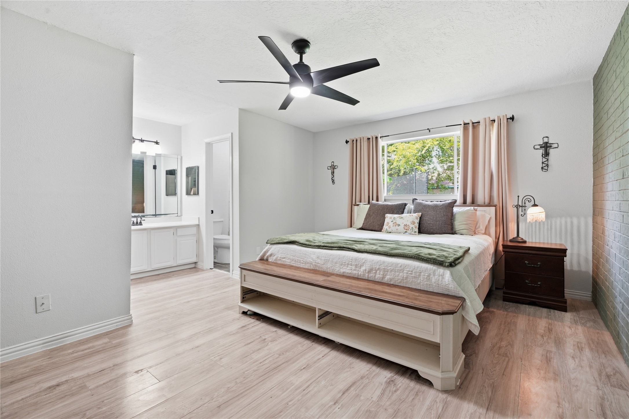 Expansive primary suite with ample space for a king-size bed, wood-look flooring, large window, and an ensuite bath with dual vanities.