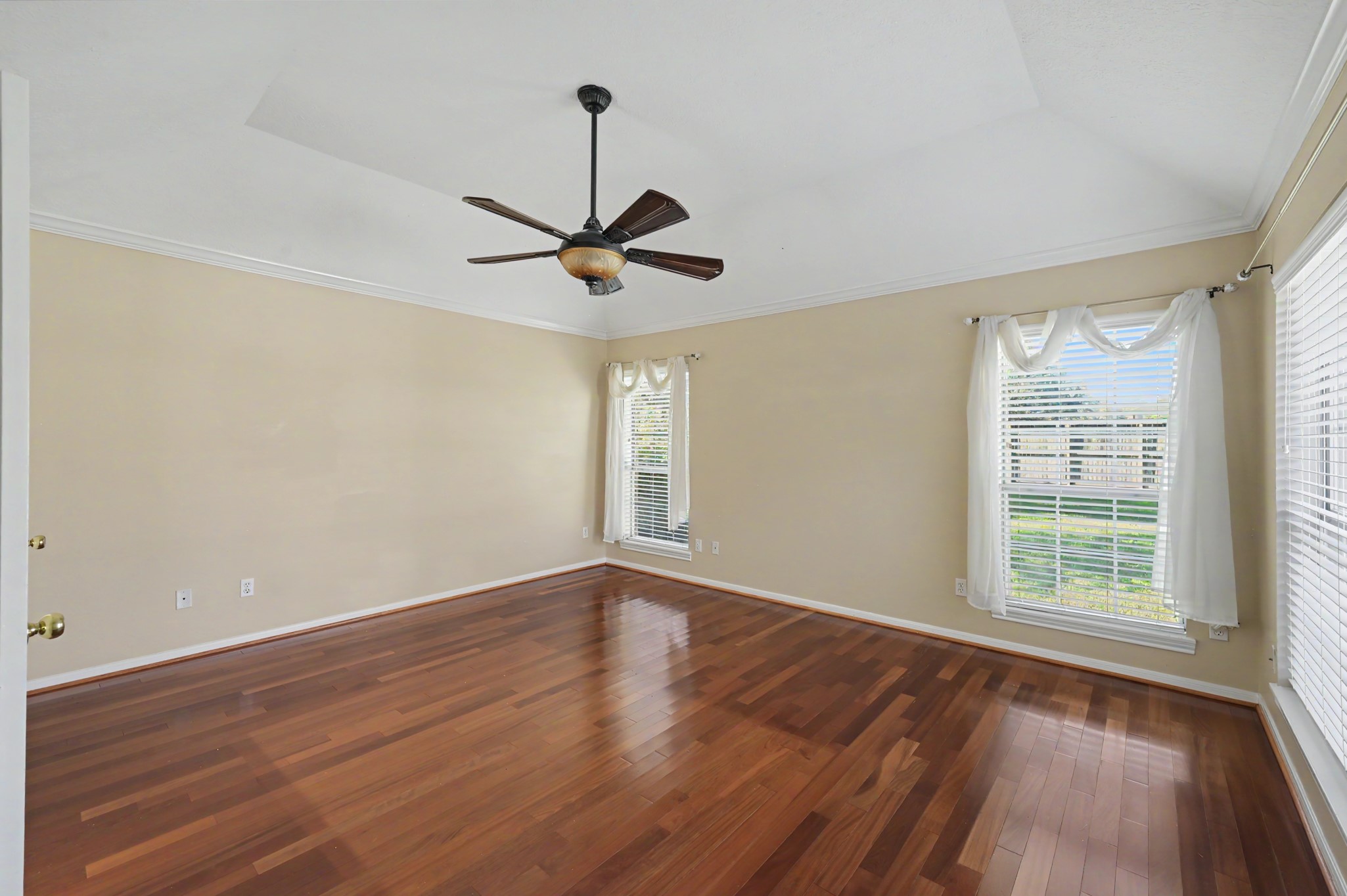 Spacious primary room with elegant hardwood floors, and large windows streaming with natural light.