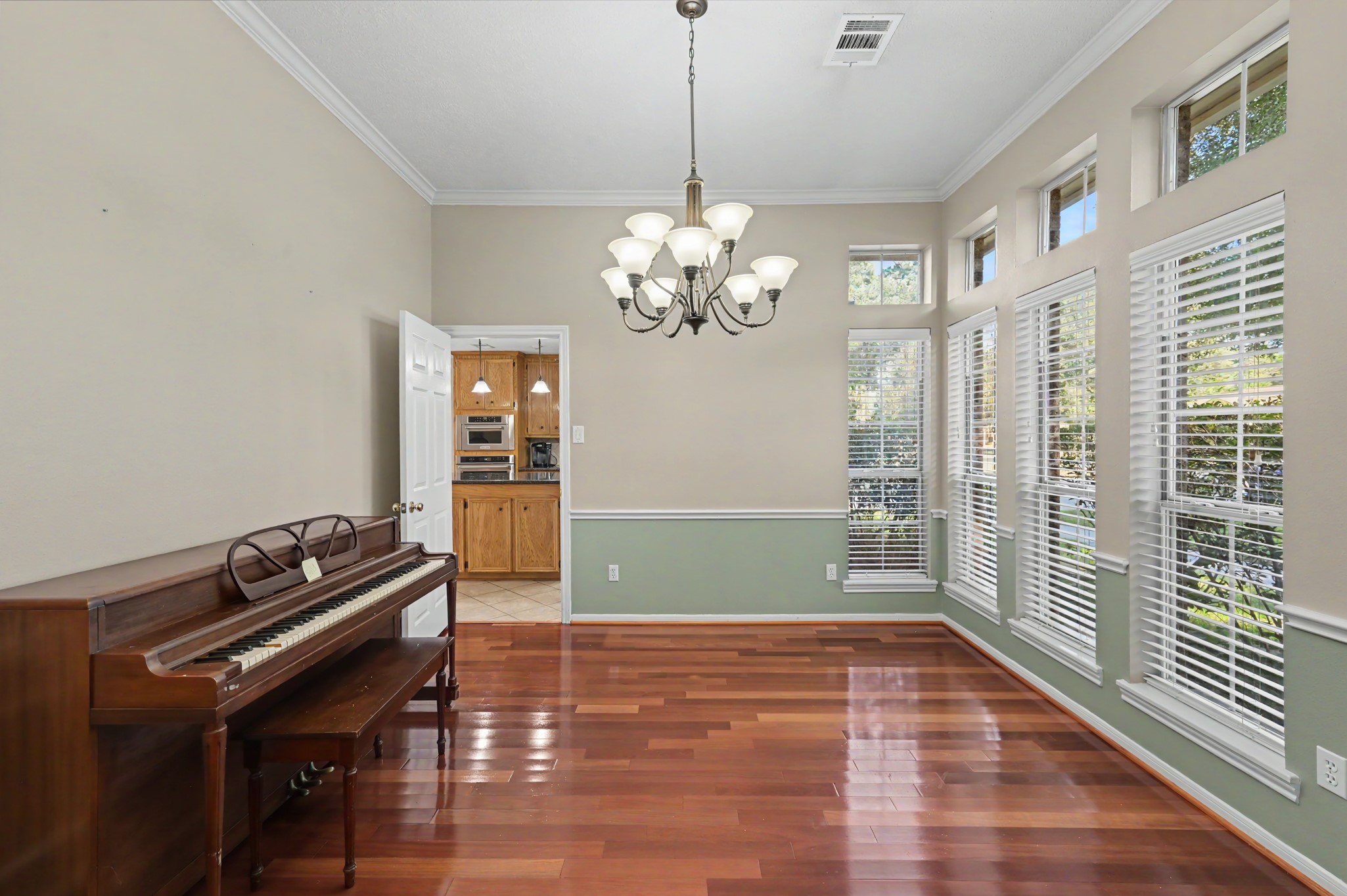 Bright dining room with elegant chandelier, large windows offering abundant natural light, and rich hardwood floors. Adjacent to the kitchen, perfect for entertaining.