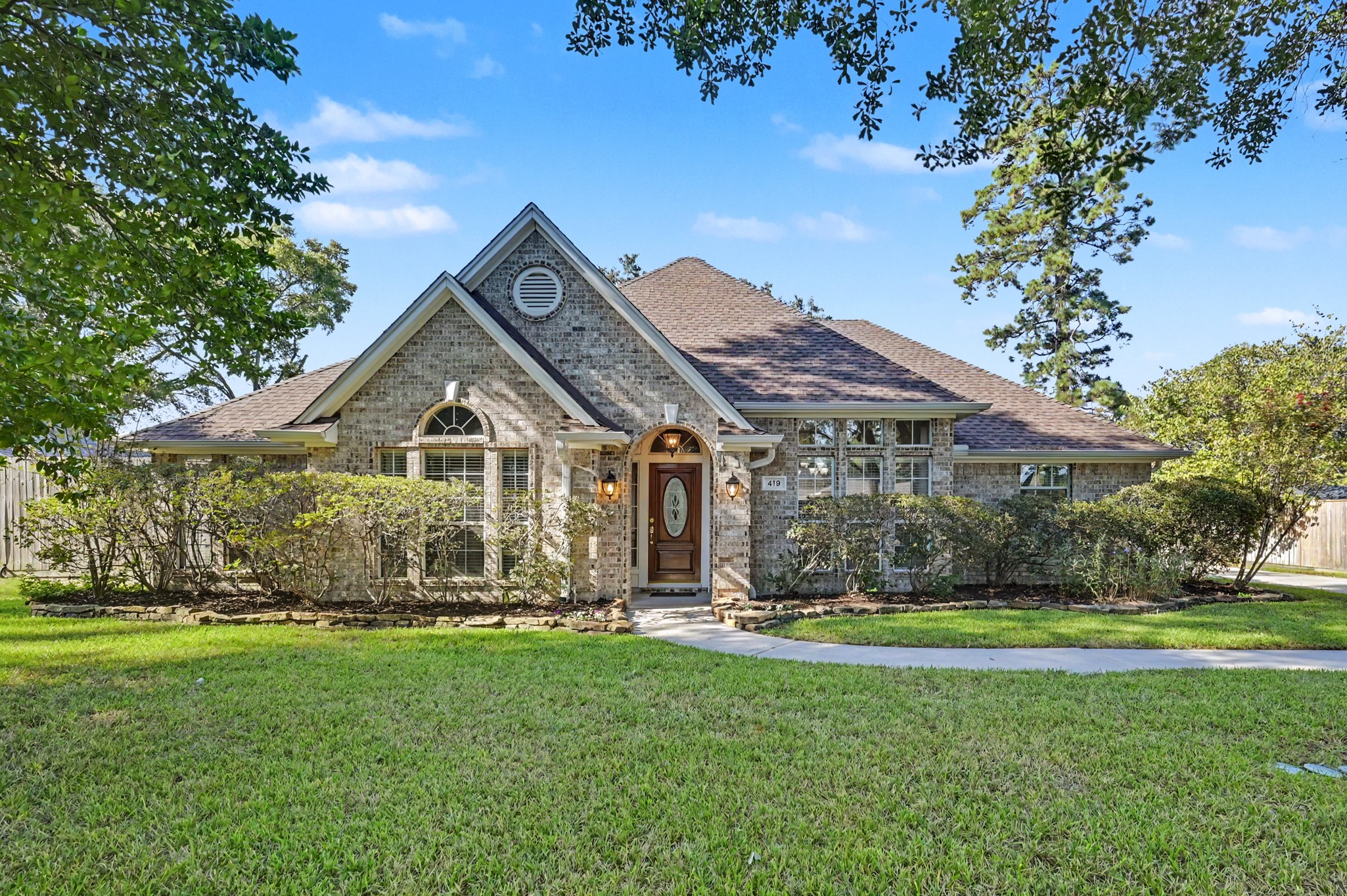 Charming brick home with arched windows and a welcoming front entry, surrounded by lush greenery and a well-maintained lawn.