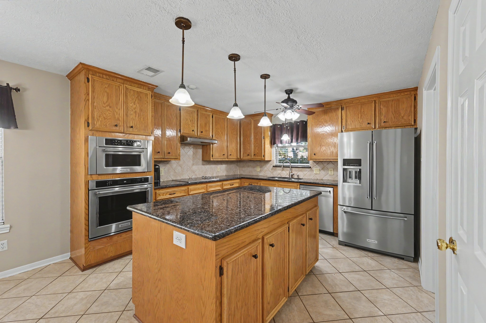 Another view of the kitchen boasting tons of storage, beautiful granite countertops, a central island, and Kitchenaid stainless steel appliances.