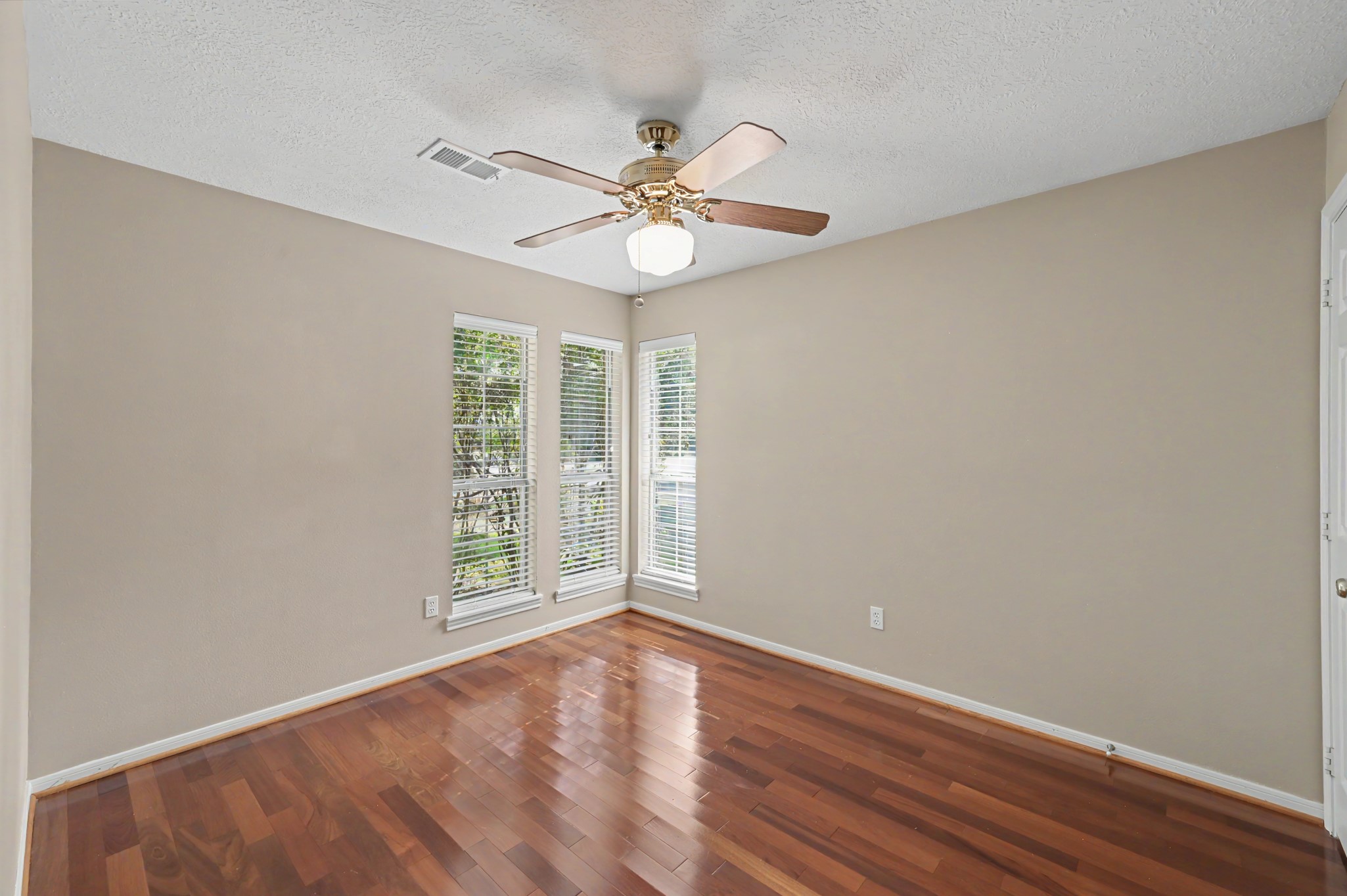 Bright and inviting bedroom three, featuring hardwood floors, and large windows that bathe the room with plenty of natural light.