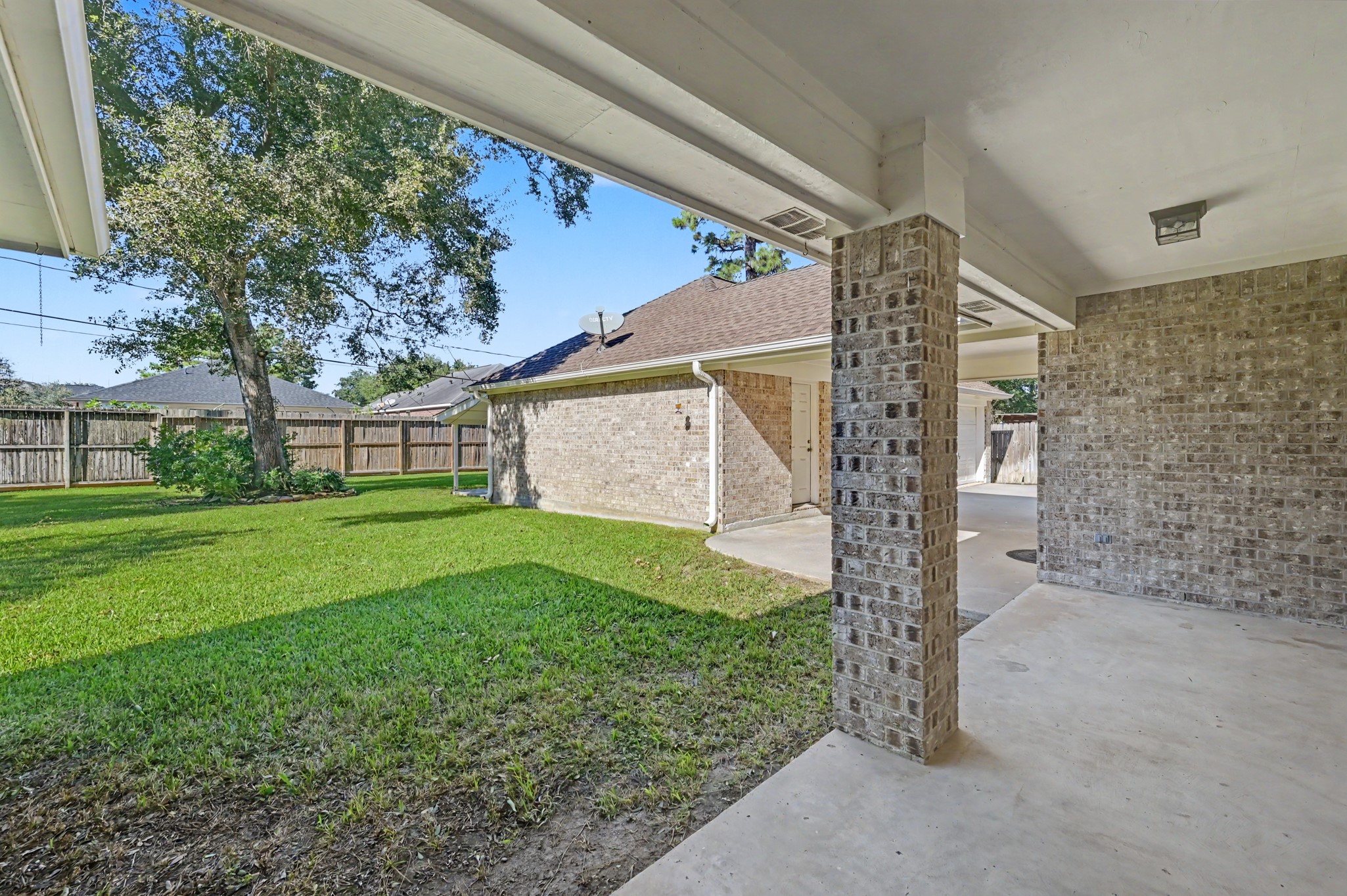 Charming covered patio overlooking a spacious backyard with lush green grass and mature trees, perfect for outdoor relaxation and entertaining.