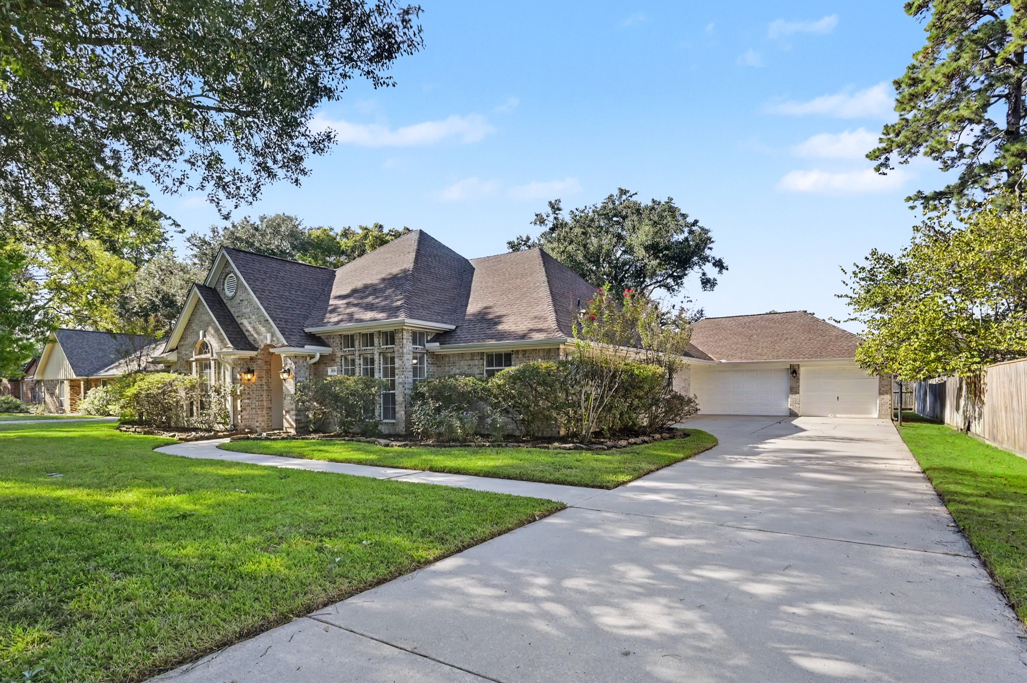 Charming home with a classic brick exterior, nestled on a spacious lot with lush greenery and mature trees. The long driveway leads to a large 3-car garage, offering ample parking space.