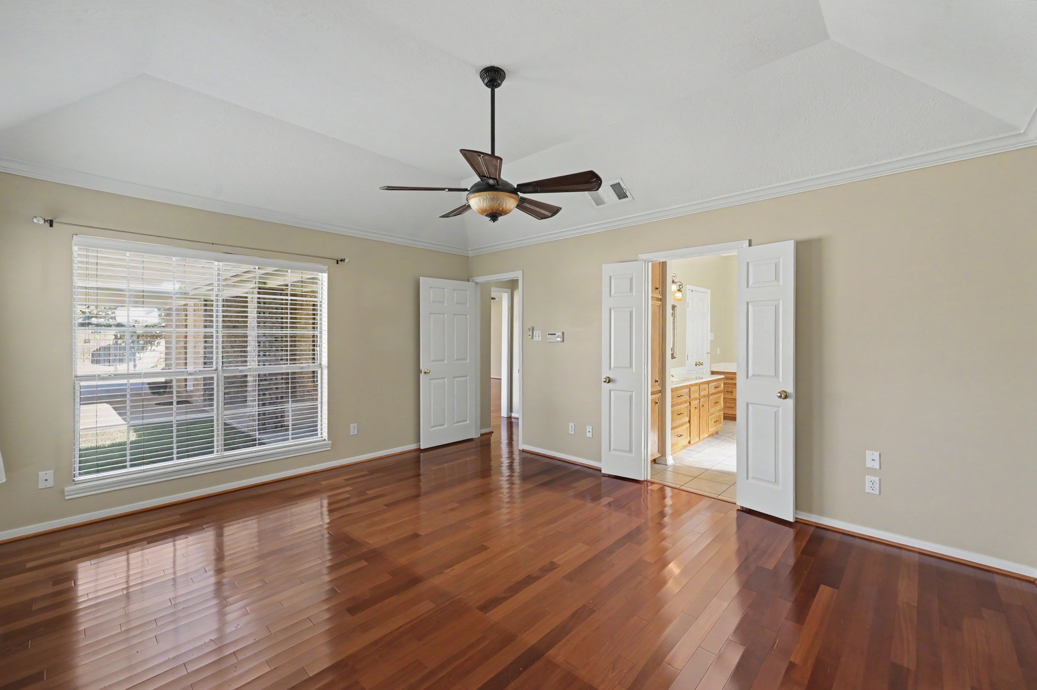 Another view of primary bedroom with gleaming hardwood floors, large windows streaming with natural light. Double doors lead to an en-suite bathroom, enhancing both style and convenience.
