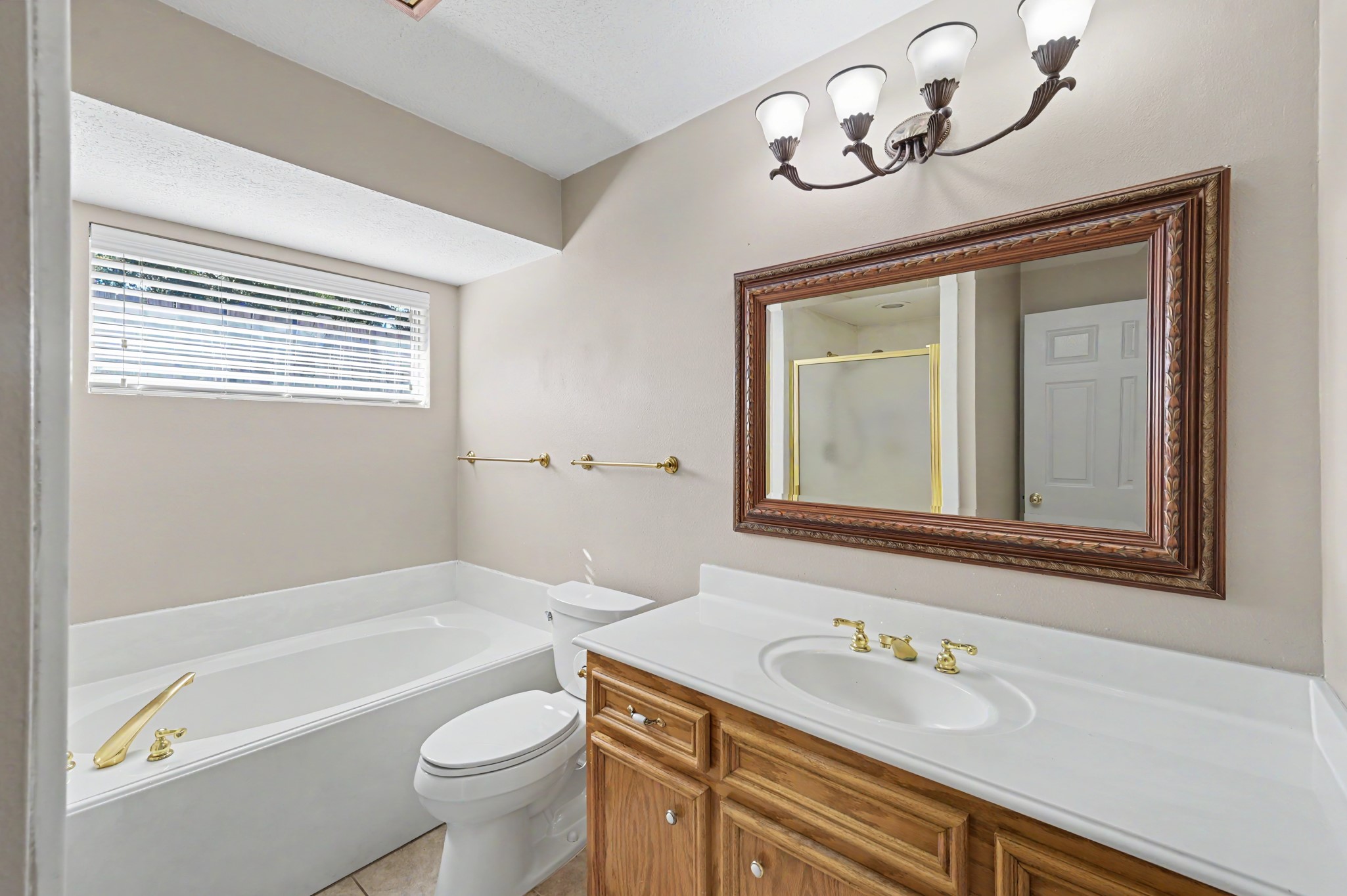 Guest bathroom featuring a spacious bathtub, separate shower, a vanity with gold fixtures, and a large framed mirror, complemented by natural light from the window.