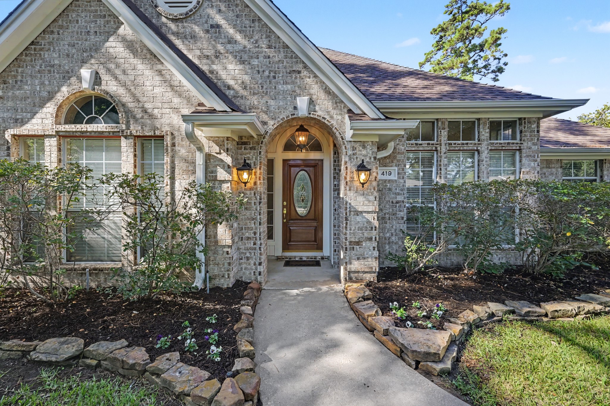 Beautiful well maintained brick home surrounded by lush landscaping and stone-bordered flower beds.