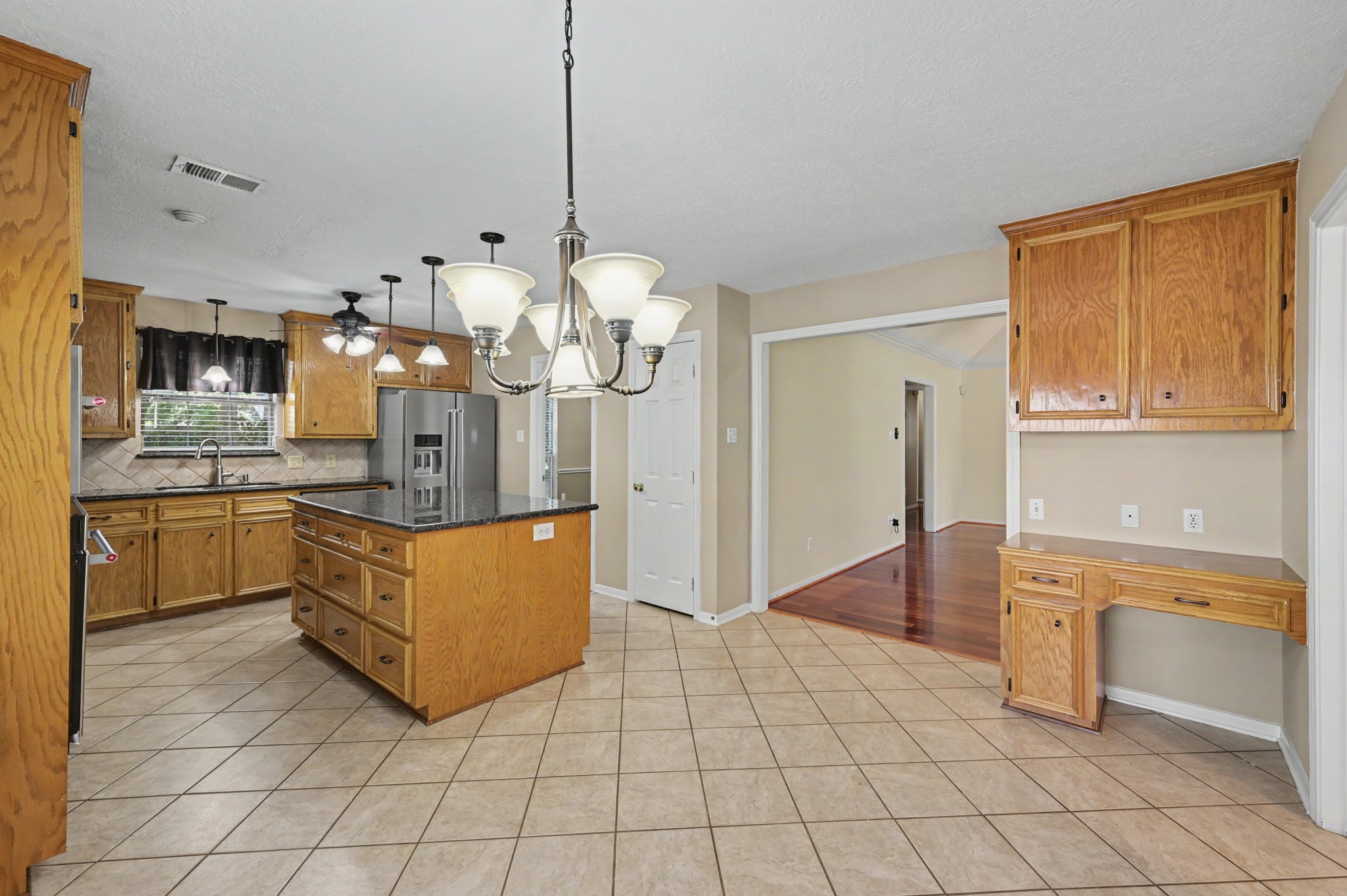 Light & bright kitchen with warm wooden cabinetry, a large central island with granite countertops, and modern Kitchenaid stainless steel appliances.
