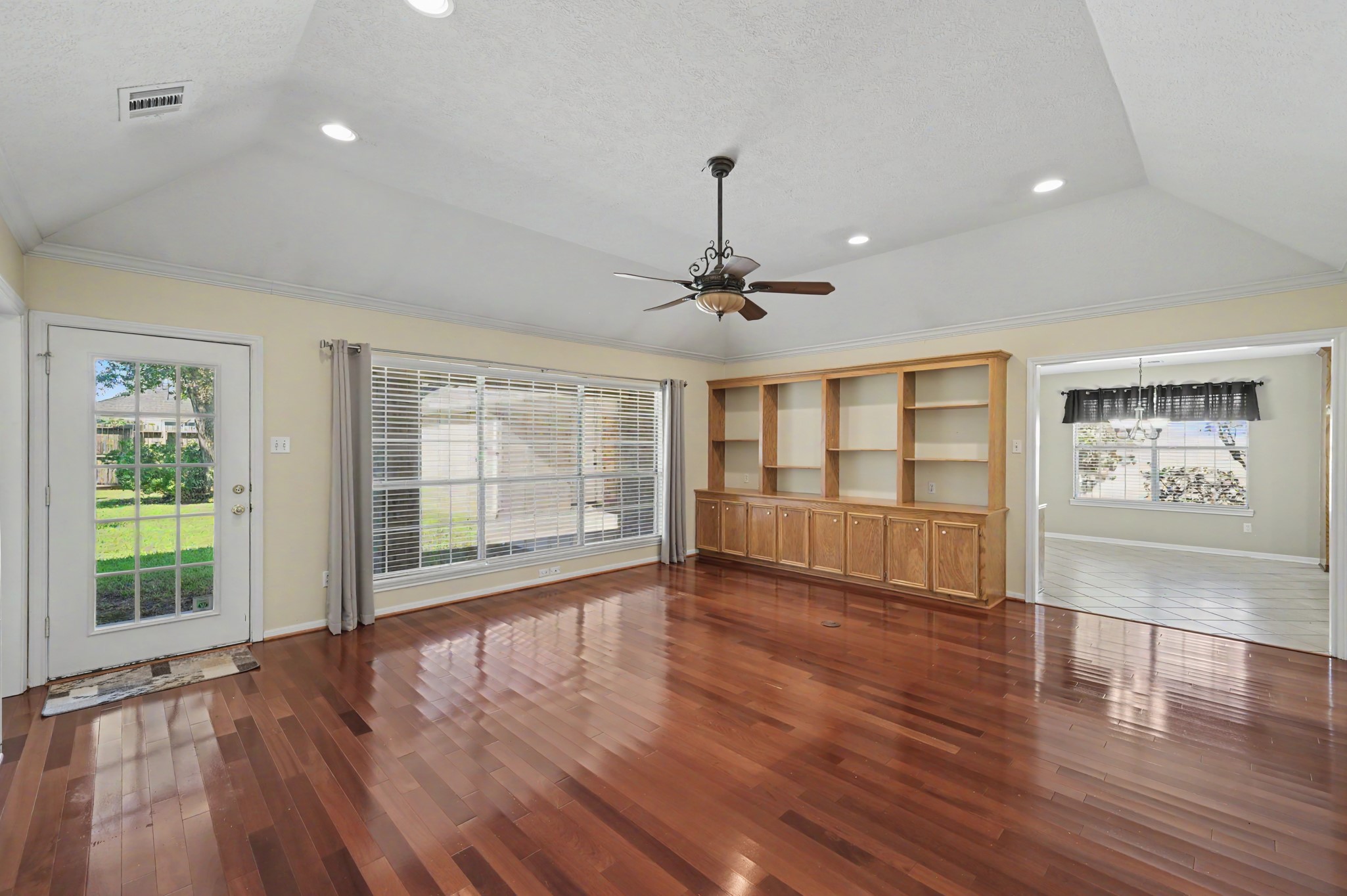 Spacious living area with rich hardwood floors, large windows for natural light, and beautiful built-in shelving, seamlessly connecting to a bright kitchen space with plenty of room for casual dining.
