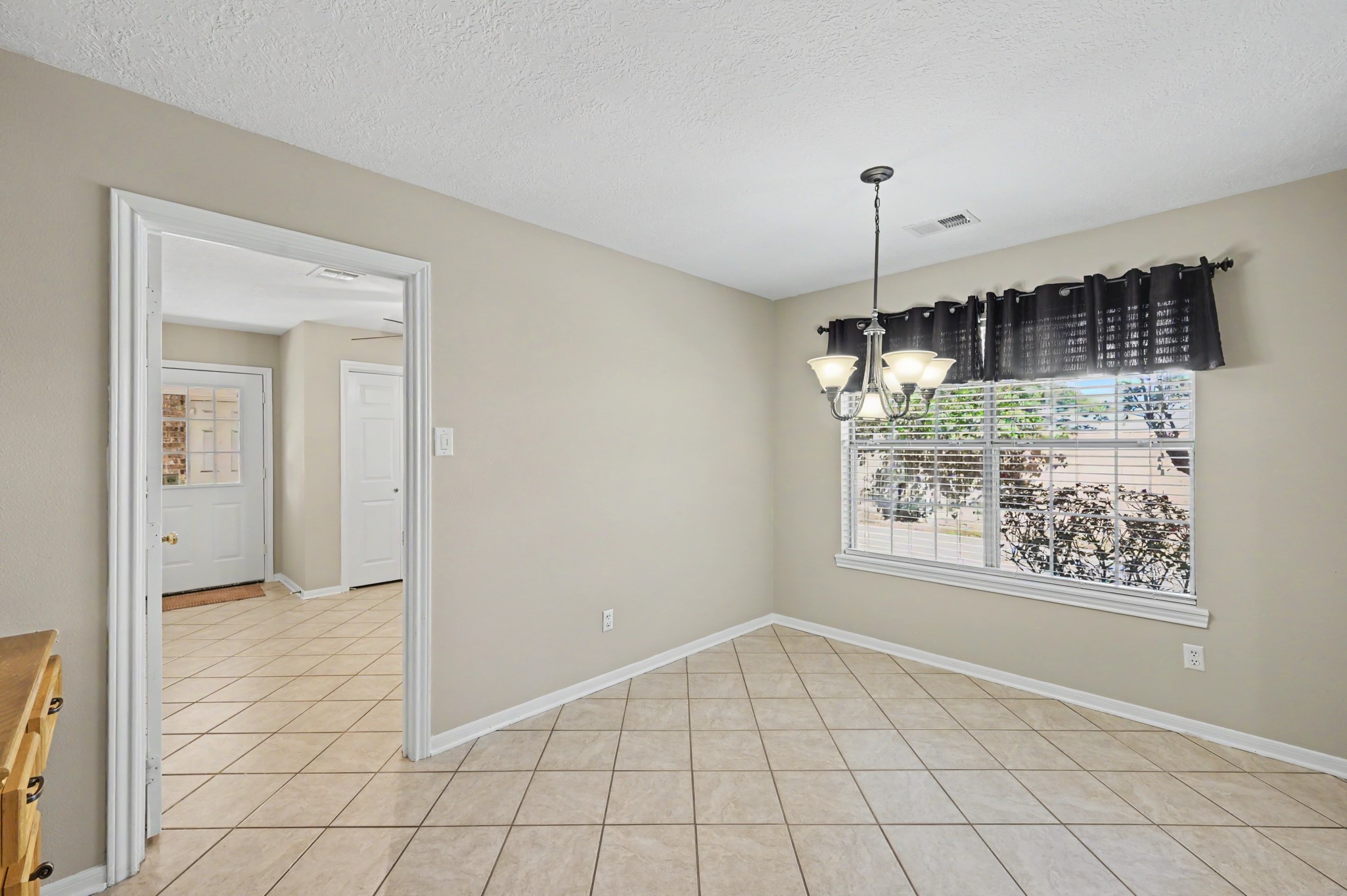 Bright dining area with tiled floors, and a large window offering natural light and garden views. Doorway leads into a large office space with tons of storage and a laundry closet, along with a backyard exit.