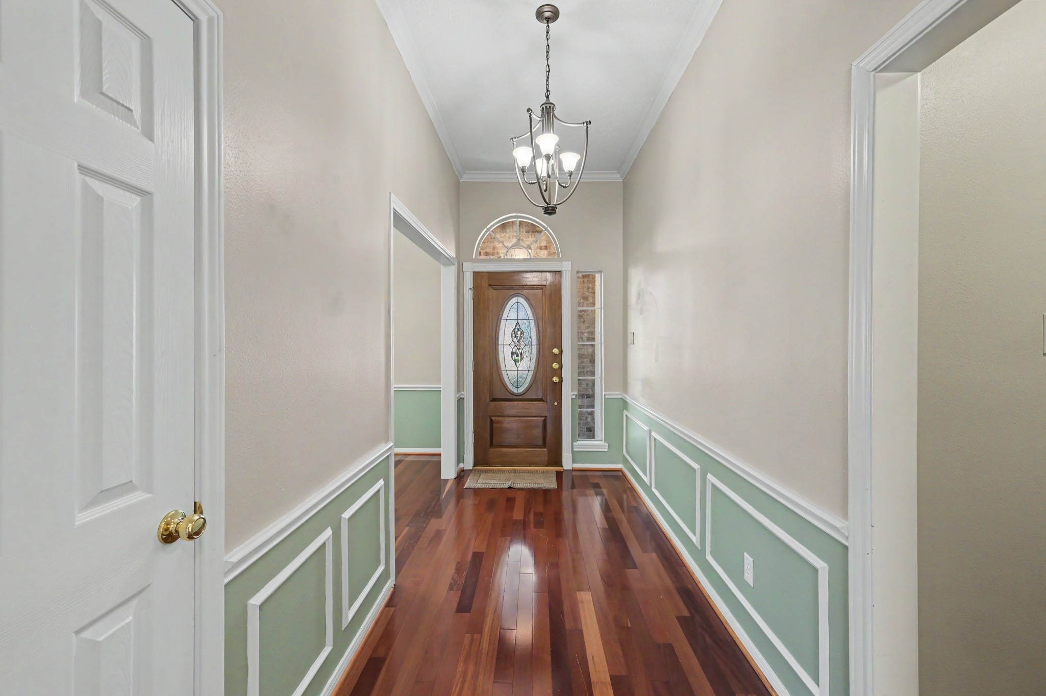 Elegant entryway featuring rich hardwood floors, wainscoting, and a decorative chandelier leading to a beautiful wooden front door with glass insets.