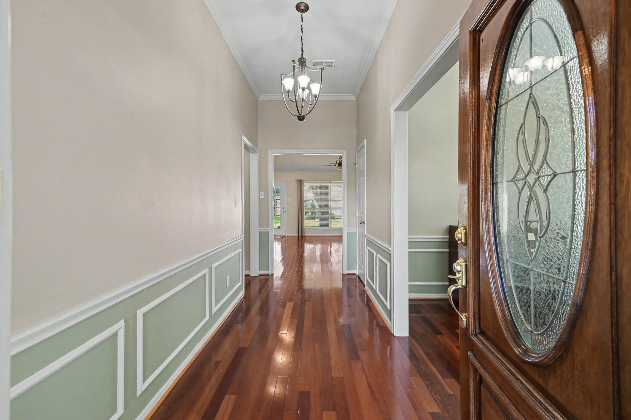Elegant entryway featuring rich wood flooring, decorative wainscoting, and a striking glass-paneled front door, leading to a bright and inviting interior. Formal dining room on the right of the entryway.