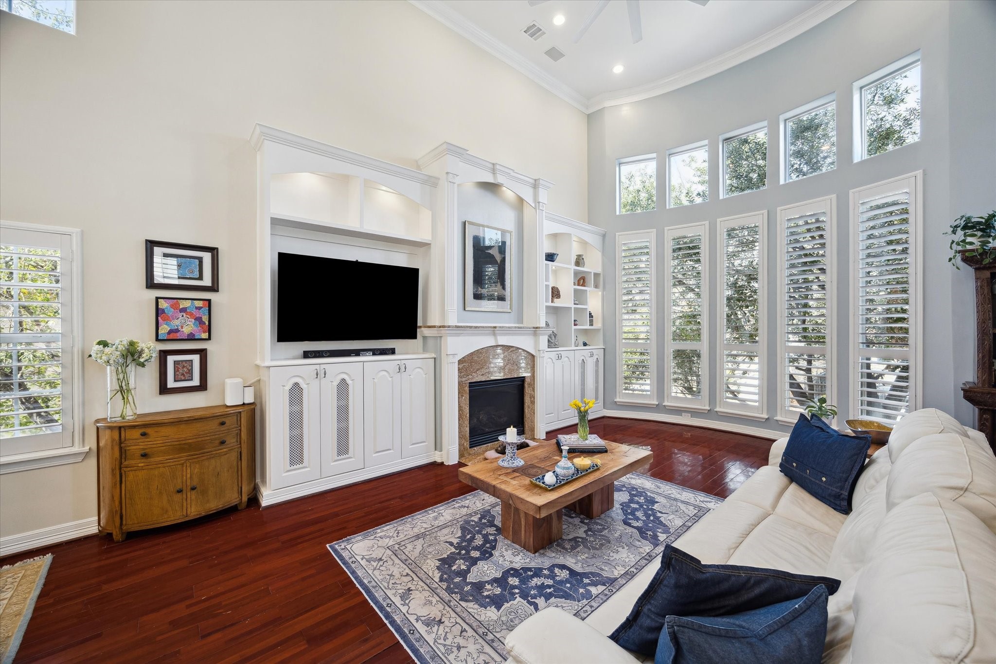 The inviting living room features high ceilings, large windows with plantation shutters, elegant built-in shelving, and wood floors. You will appreciate the privacy given by the mature tree outside and the warmth of this space.