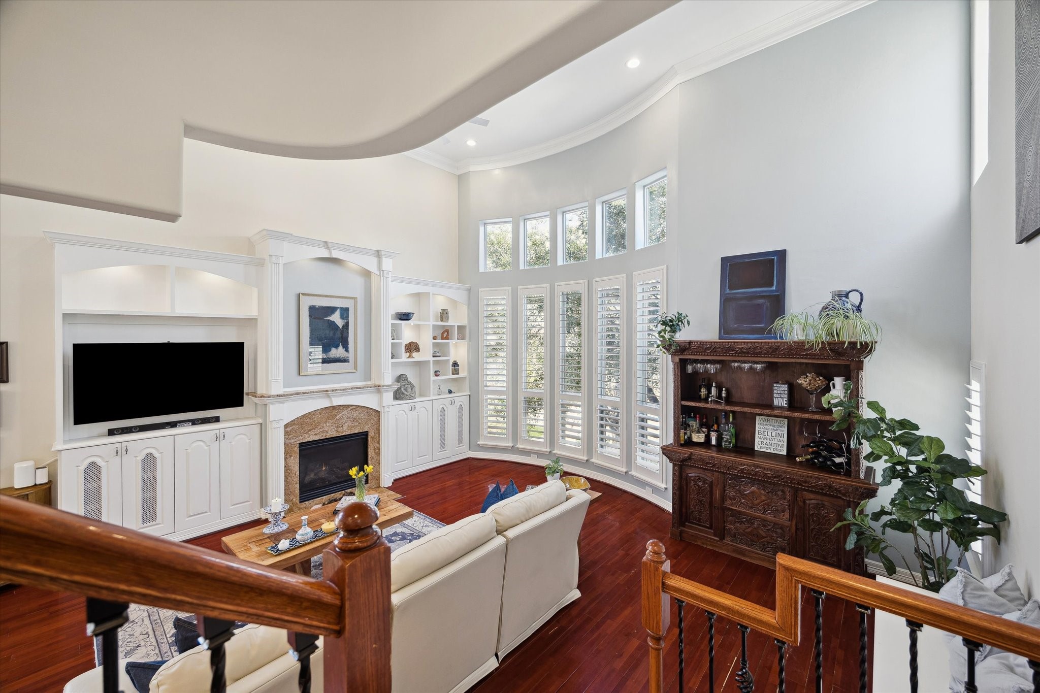 The semi bay windows with plantation shutters, built-in entertainment center, a fireplace, elegant shelving, and natural light, adds functionality with a warm ambiance.
