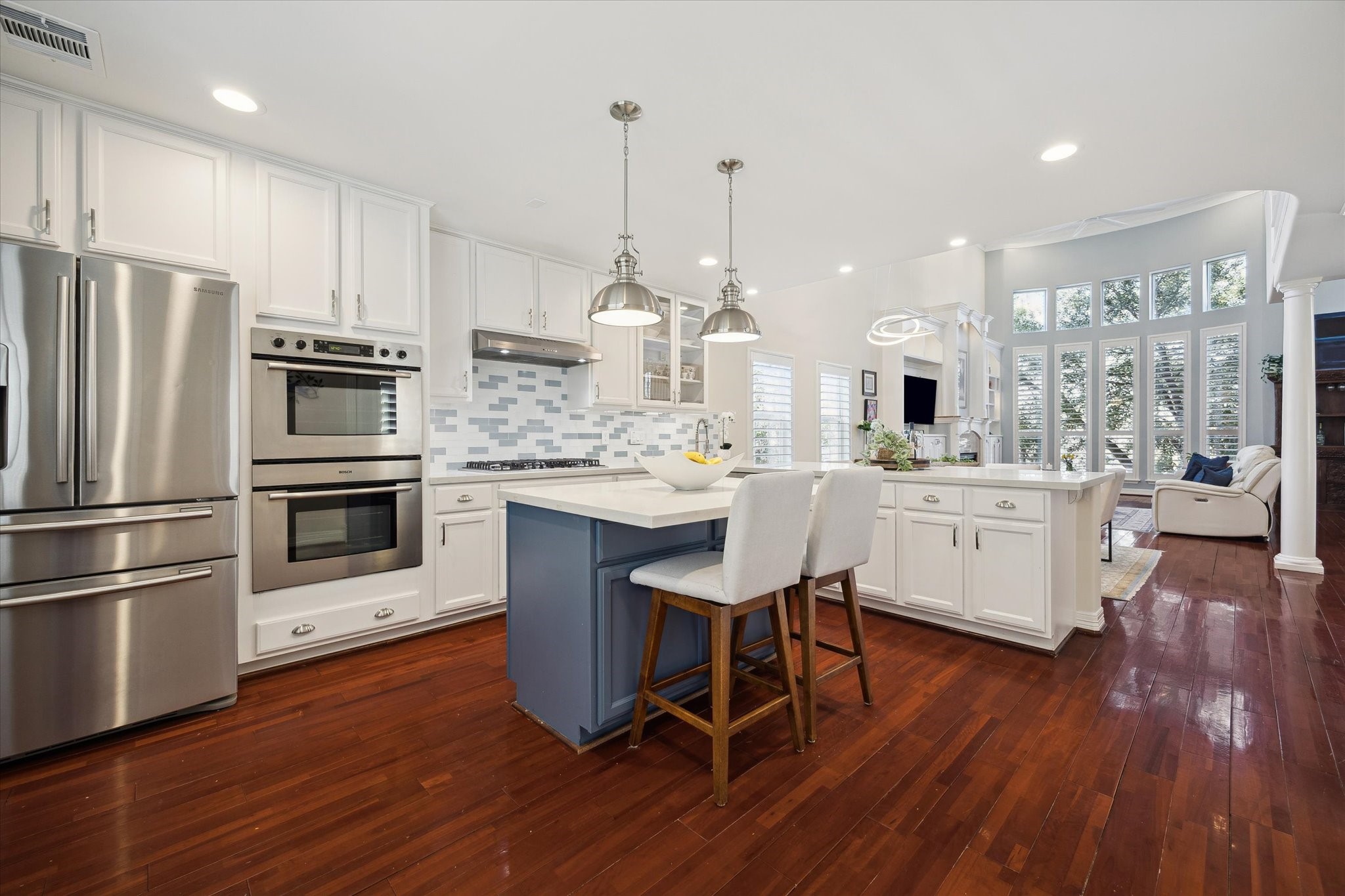This bright, open kitchen features stainless steel appliances, white cabinetry, a stylish tile backsplash, and a central island with seating.