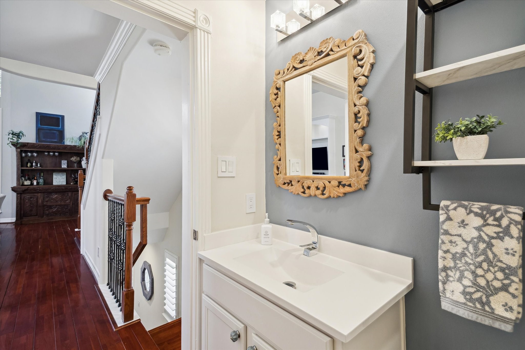 A half-bathroom tuck away for privacy, featuring a decorative mirror, modern lighting, and a sleek sink.