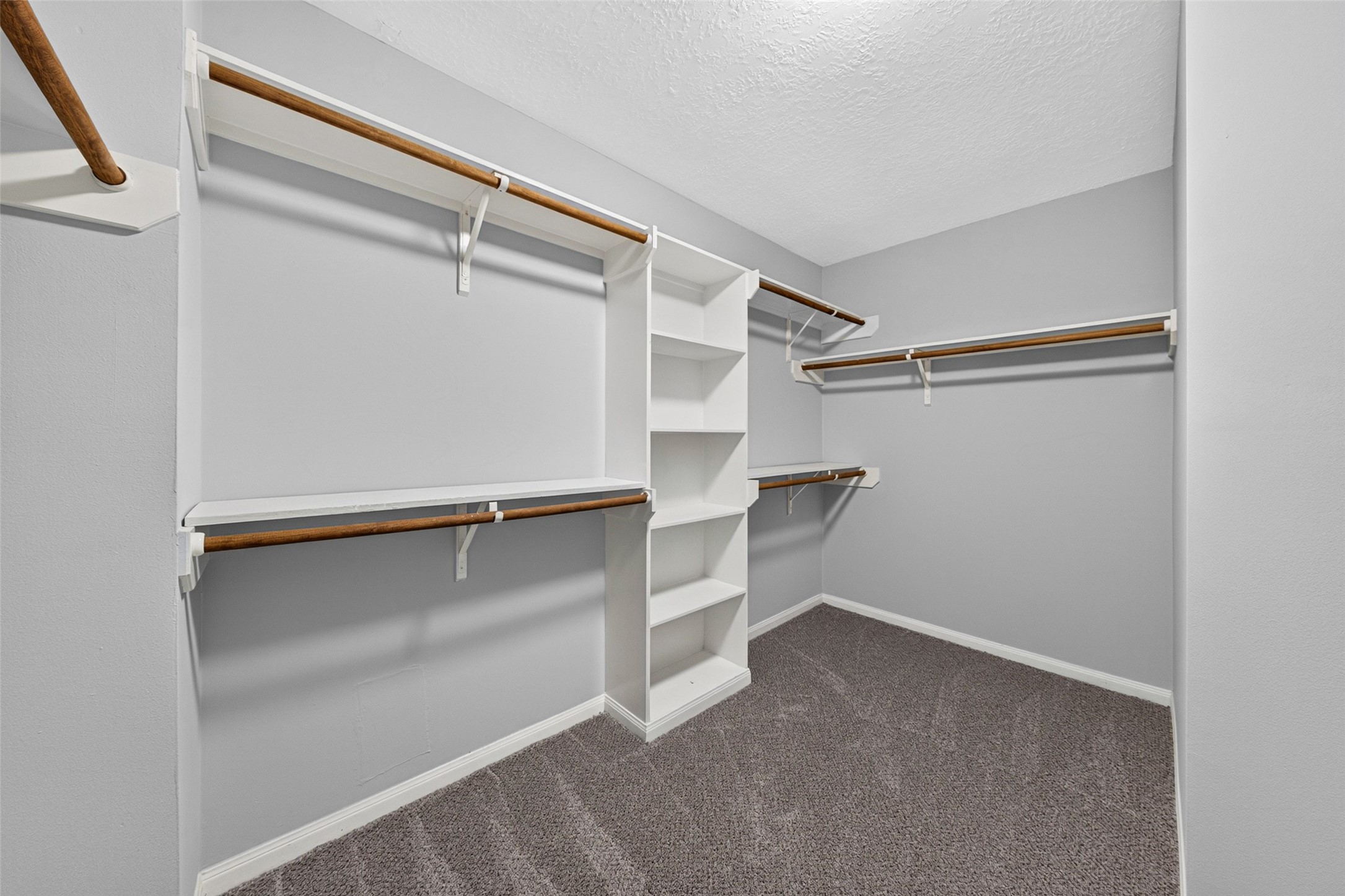 Step inside this oversized walk-in closet featuring extensive custom built-in shelving, multi-level hanging racks, and dedicated shoe display cubbies designed to keep your wardrobe effortlessly organized.