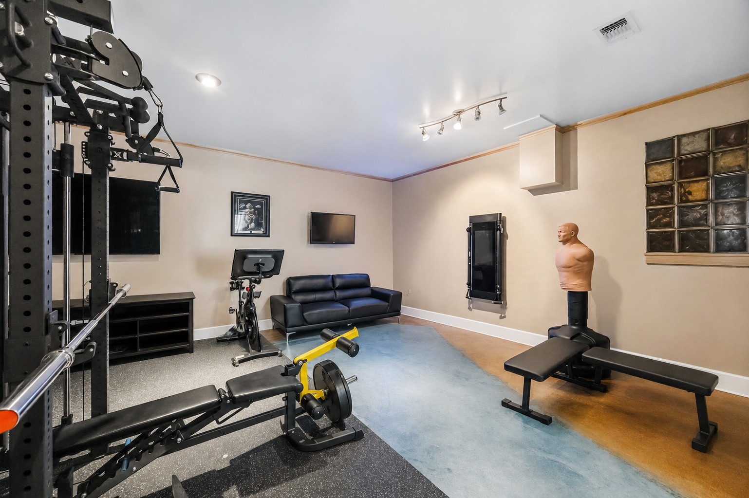 An alternate view of the flexible bonus room highlights tracked ceiling spotlights, multi-tone stained flooring, and an inset glass-block wall feature.