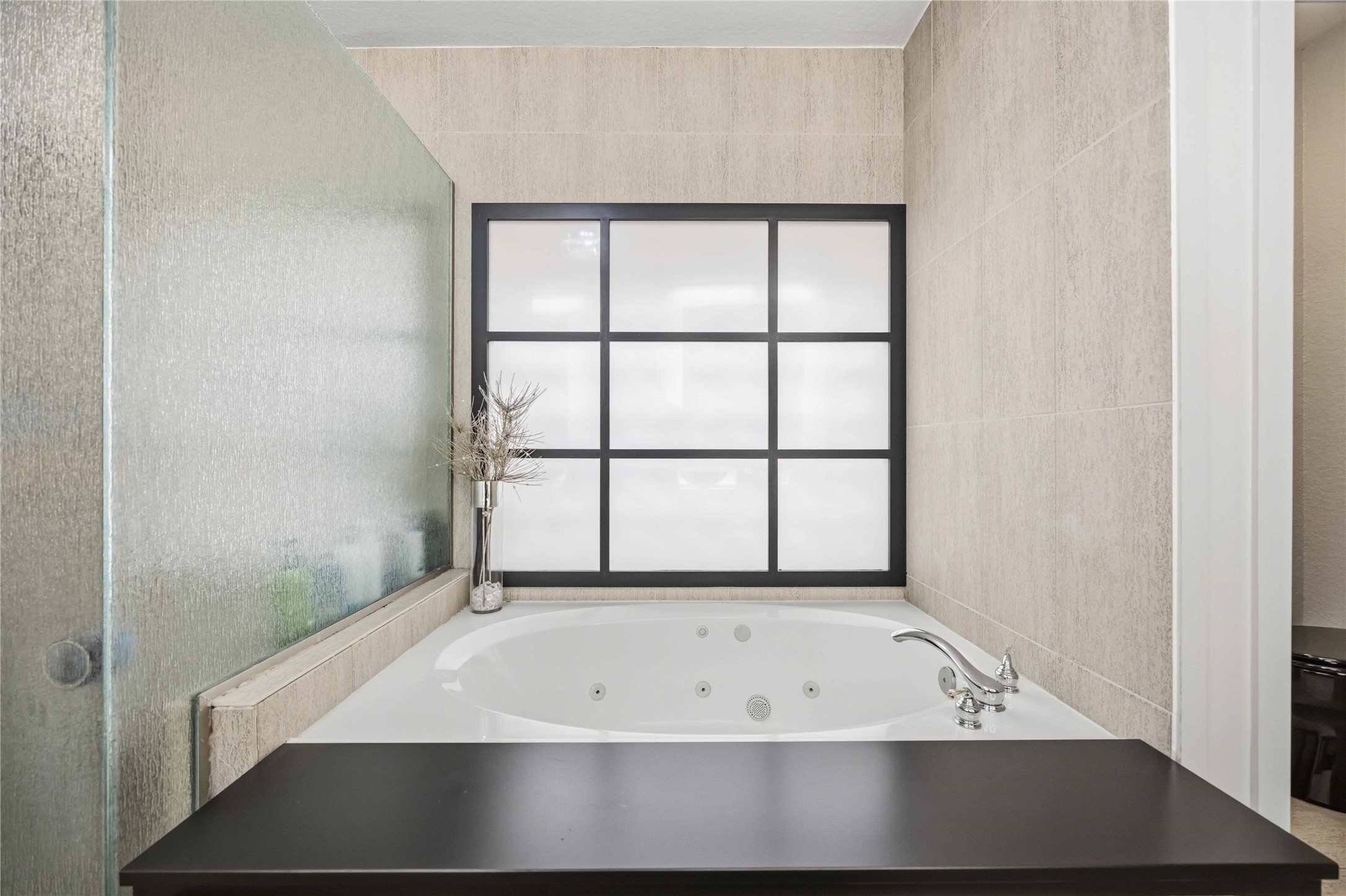 A close-up of the bathing alcove emphasizes the jetted tub's custom dark ledge wrapper and the stone-textured wall tiling.