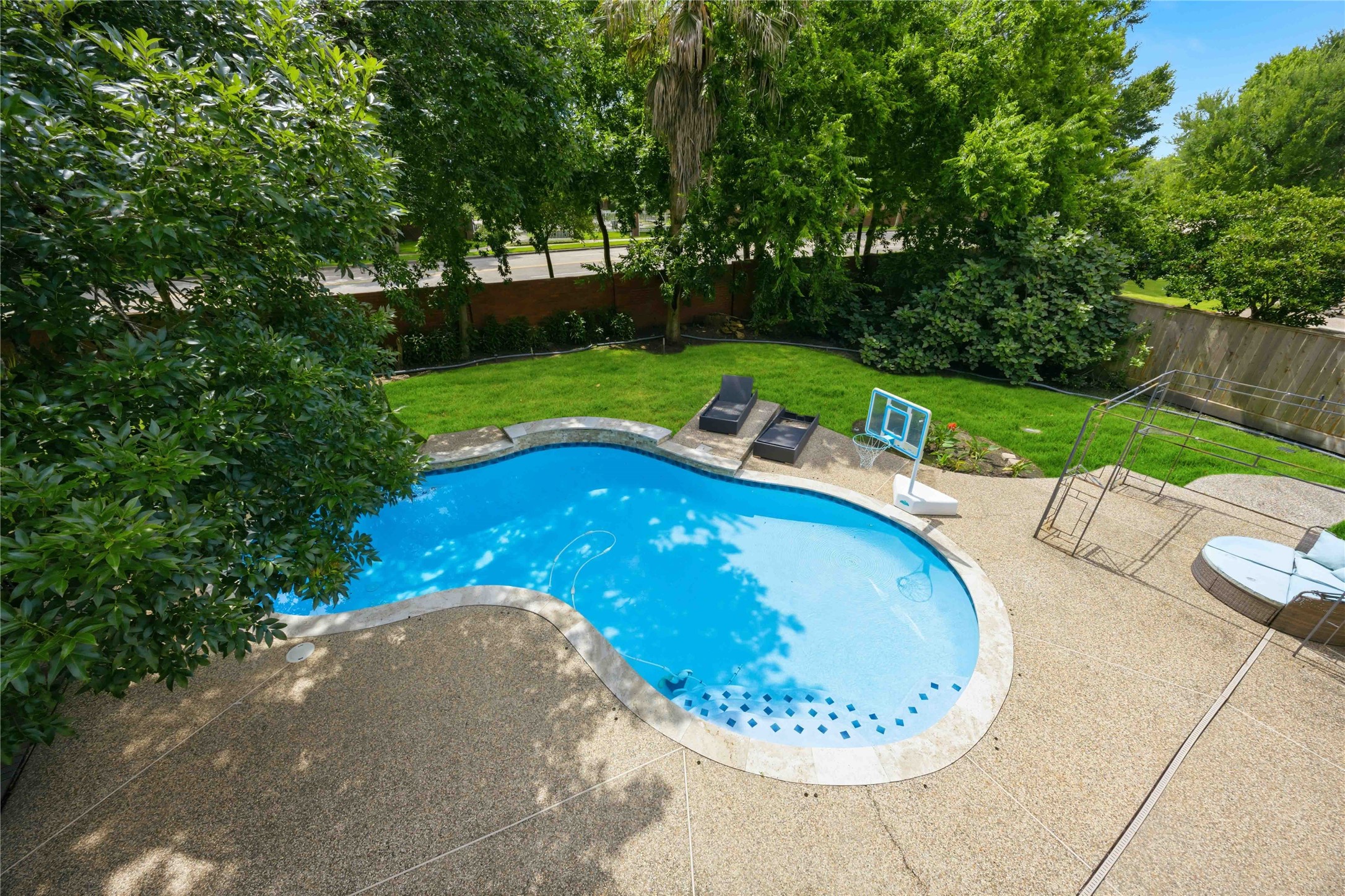 An elevated bird's-eye view reveals a custom curved in-ground swimming pool framed by an expansive concrete aggregate patio surround.
