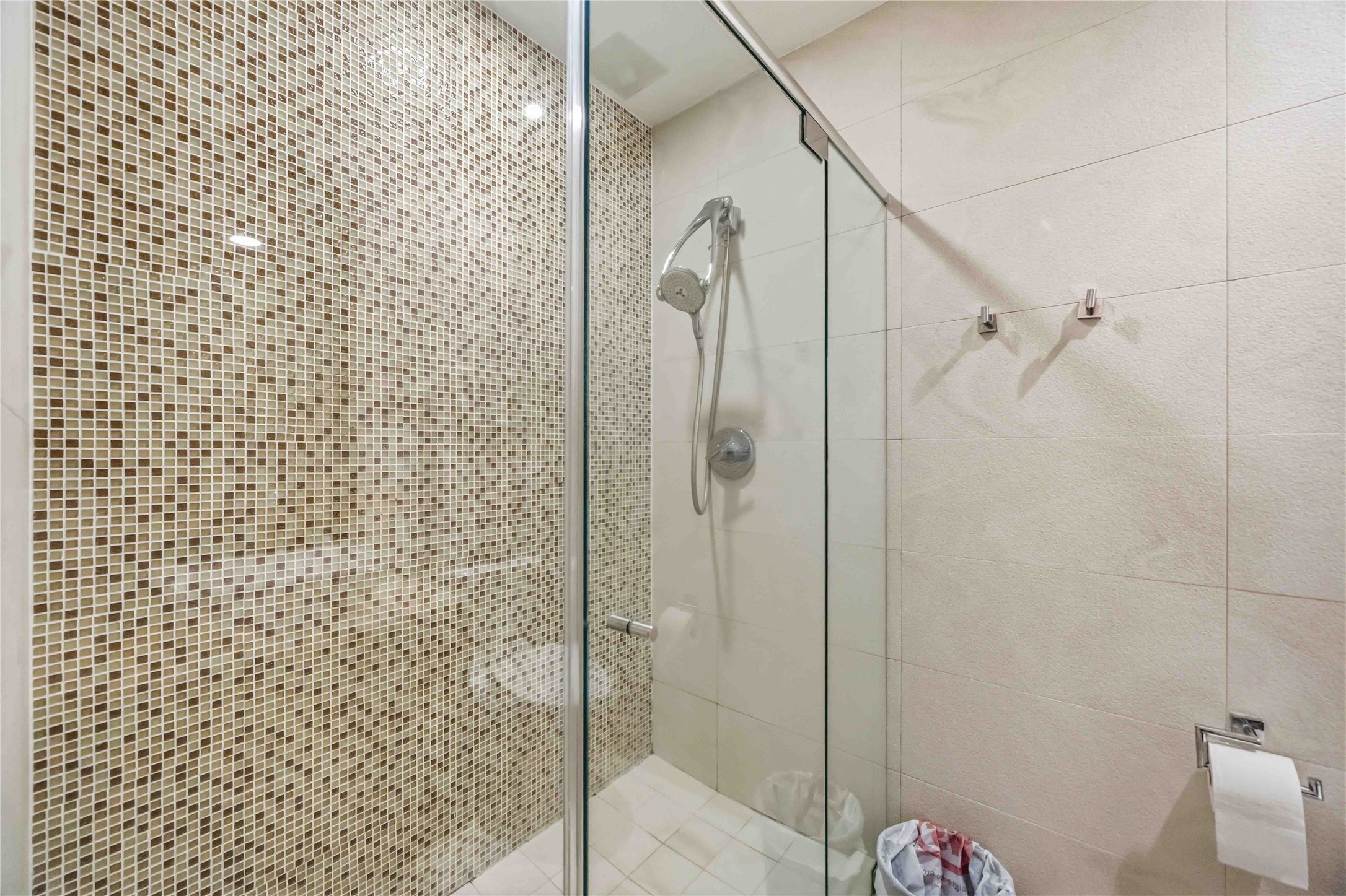 Walk-in shower with seamless glass, chrome showerhead, and mosaic tile accent wall.