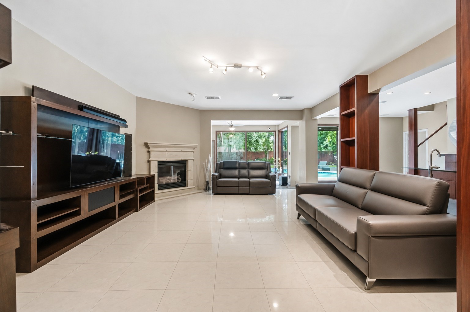 This expansive living room features a corner gas fireplace with a stone-style mantle, polished tile flooring, and integrated dark wood shelving.