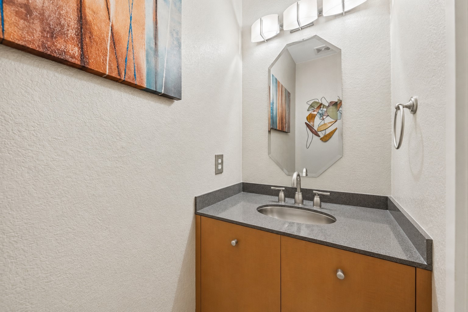 The powder room features a warm wood vanity cabinet topped with a gray stone counter, an under-mount sink, and a modern three-light wall fixture.