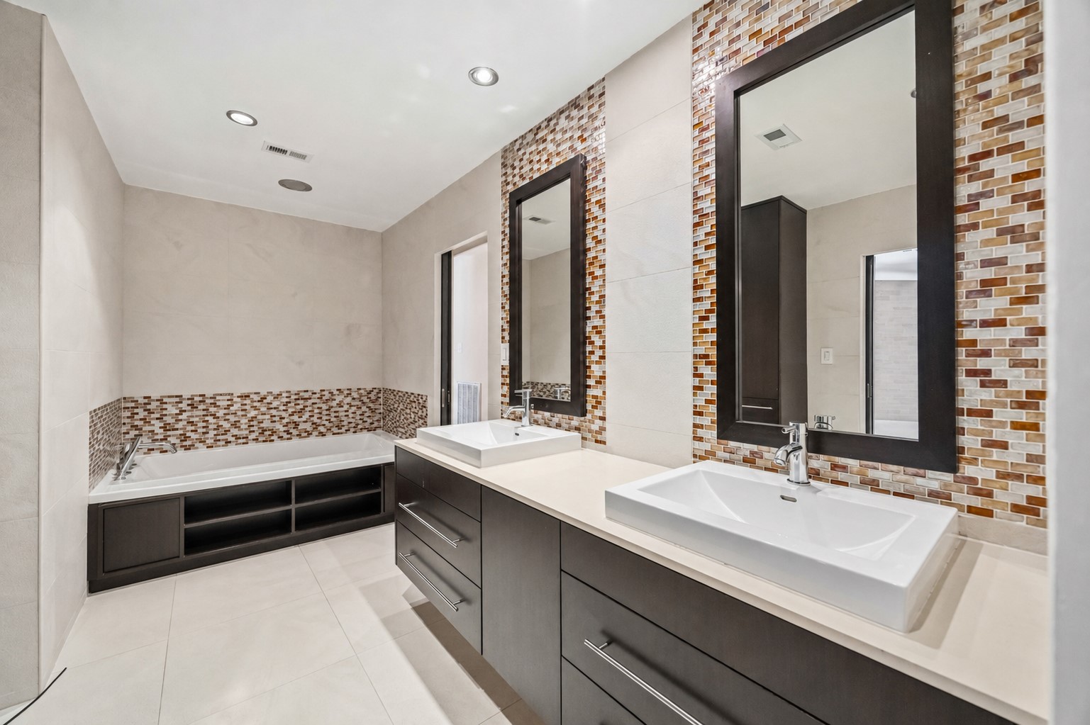 Modern full bath with a deep soaking tub, built-in shelving, dual vessel-sink vanities, and colorful mosaic tile accents.