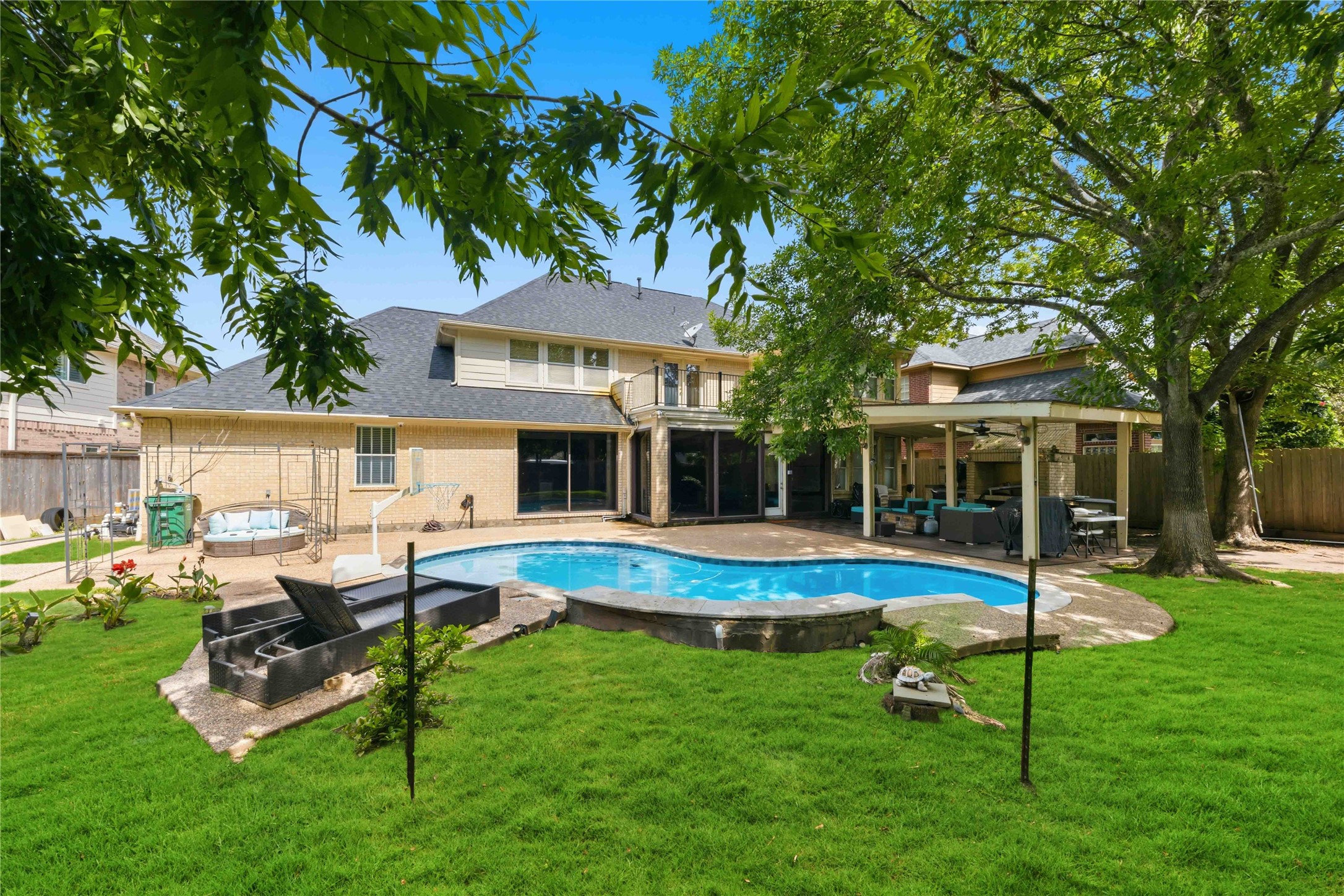 The impressive rear elevation showcases the multi-gabled roofline, an upper balcony, a covered patio wing, and an expansive pool deck.