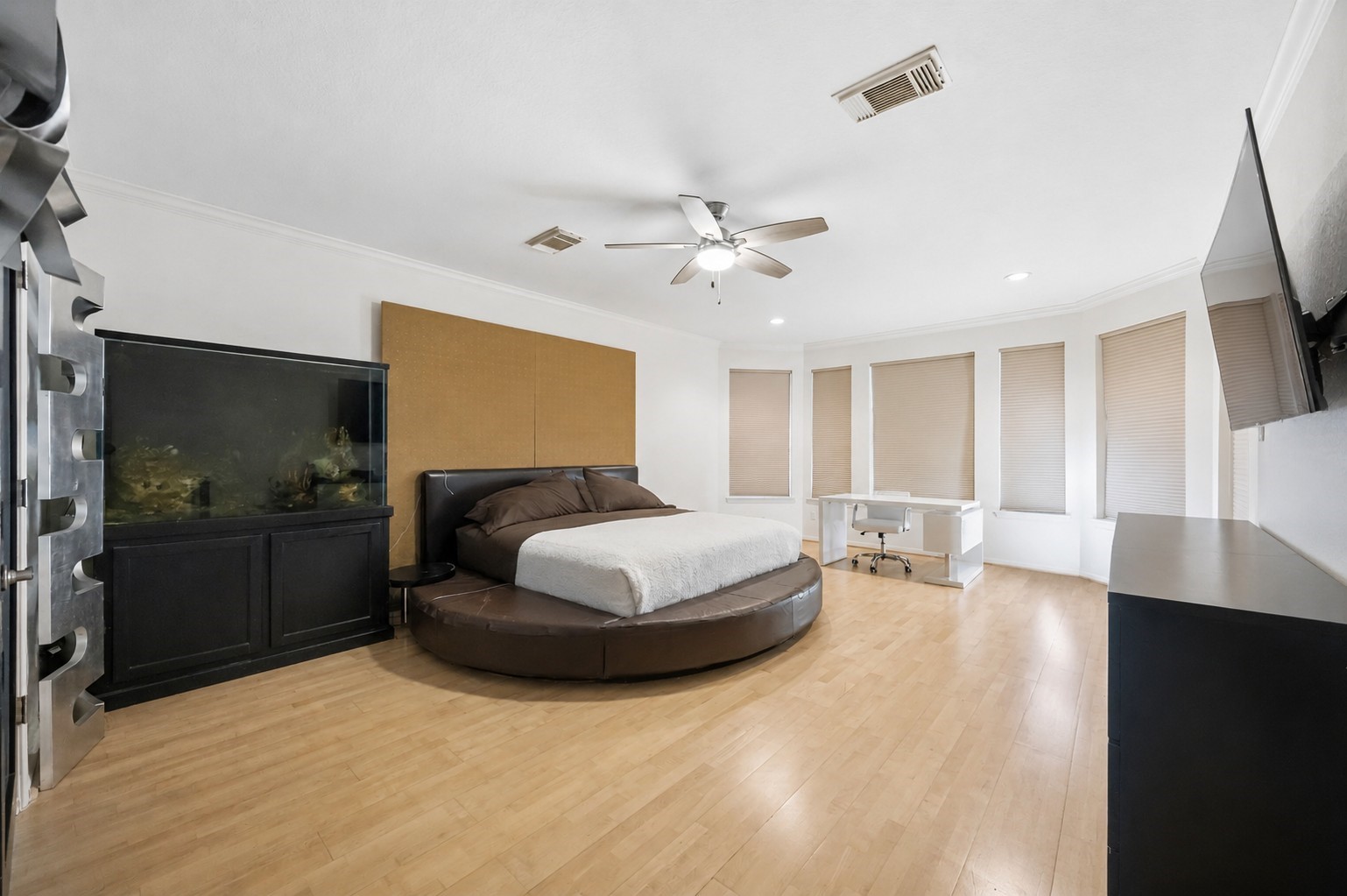 The spacious primary bedroom features smooth wood flooring, a central ceiling fan, and a curved bay window layout that welcomes natural light.