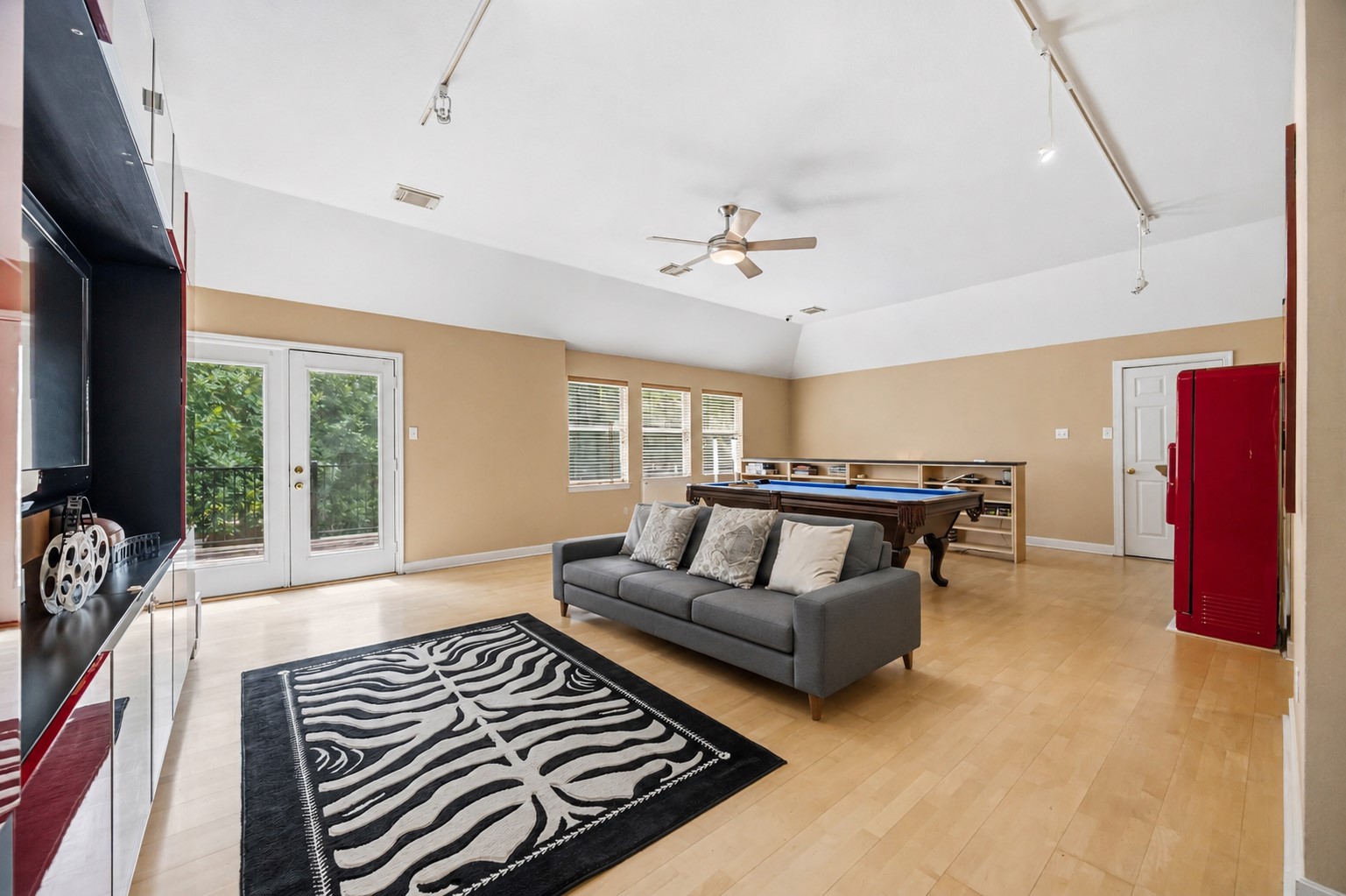 The expansive upper-level game room boasts vaulted ceilings, track lighting, light wood floors, and double glass doors that open to a private balcony.