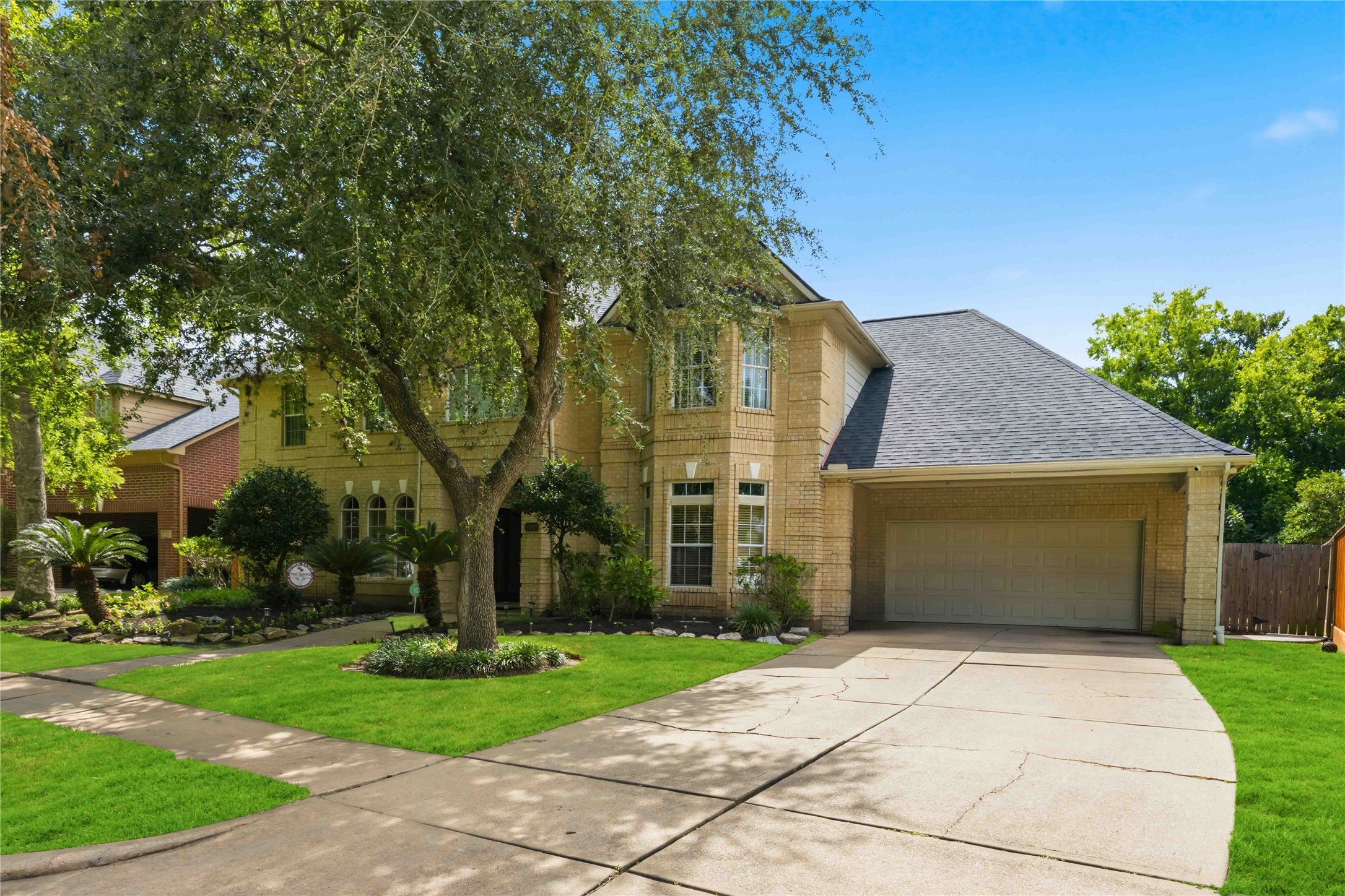 A wide concrete driveway leads up to an attached two-car garage, showcasing the home's multi-gabled roofline and manicured front lawn.