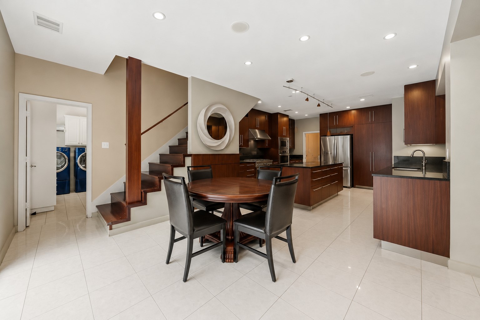 An open-concept dining space flows into the kitchen area, featuring light tile flooring and a view of a wooden staircase built into the wall.