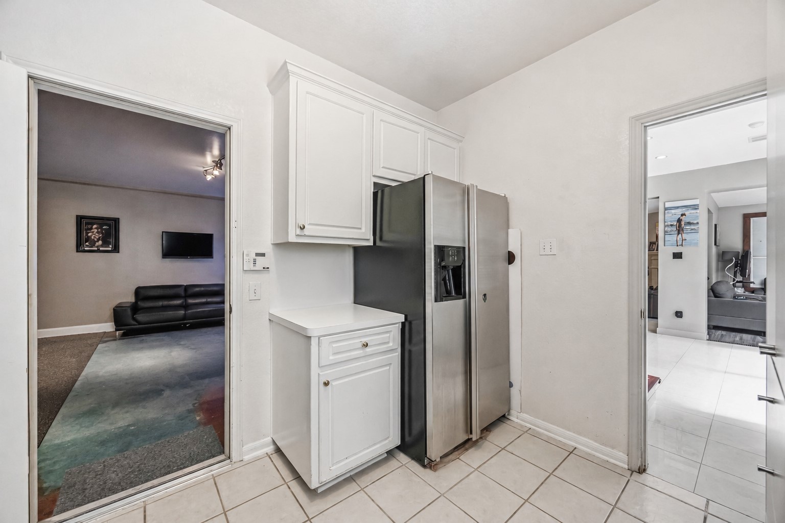A practical transition space offers white cabinetry with a light countertop alongside tile floors and an open doorway leading into the dedicated media room.