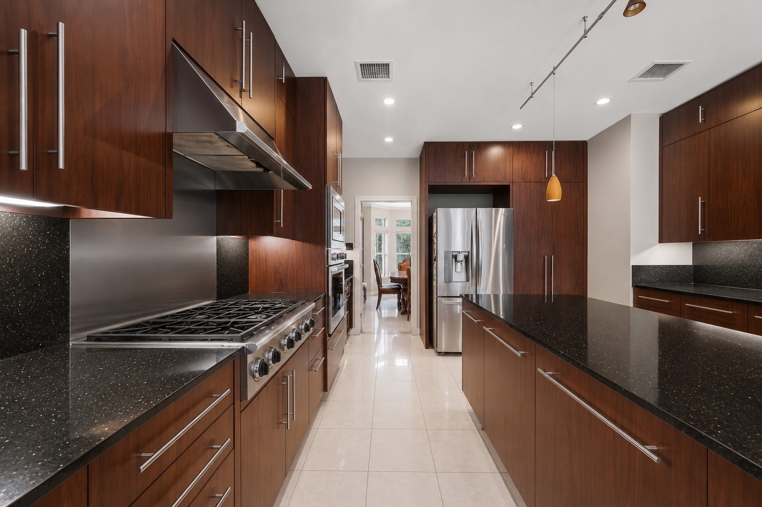 This sleek culinary space features premium stainless steel appliances, a professional-grade gas range with a matching vent hood, and a continuous stone backsplash.