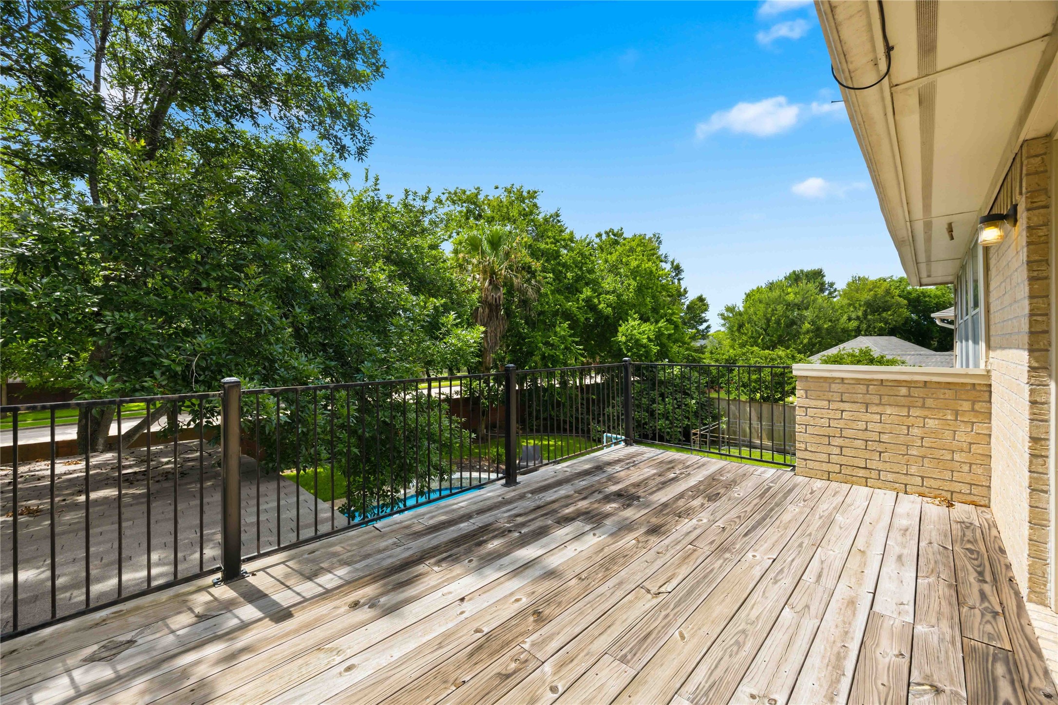 An upper-level wooden sun deck features a black metal safety railing and views overlooking the backyard greenery.