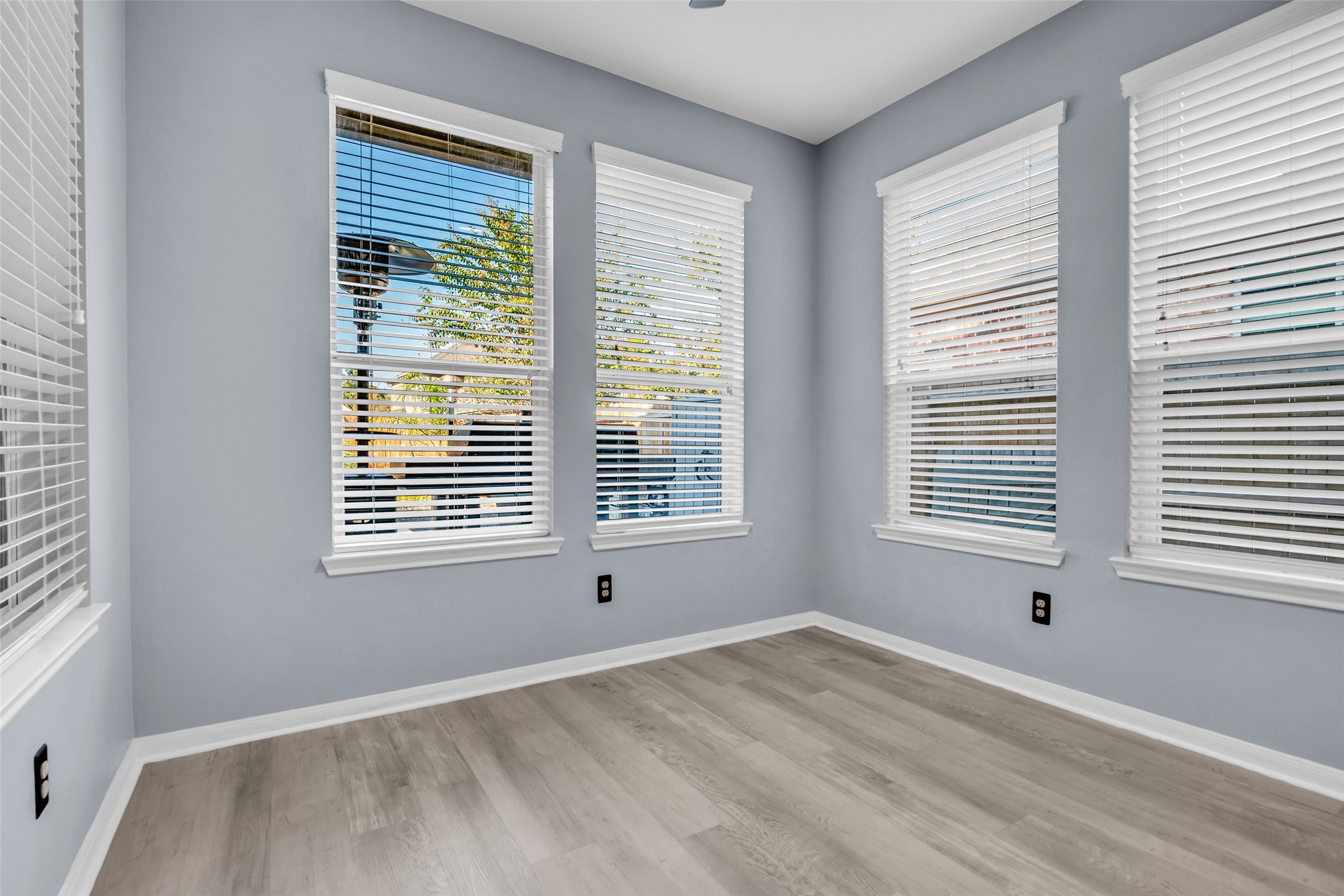 Bright and airy sunroom featuring large windows with blinds, offering ample natural light and serene views, complemented by elegant LVP flooring.