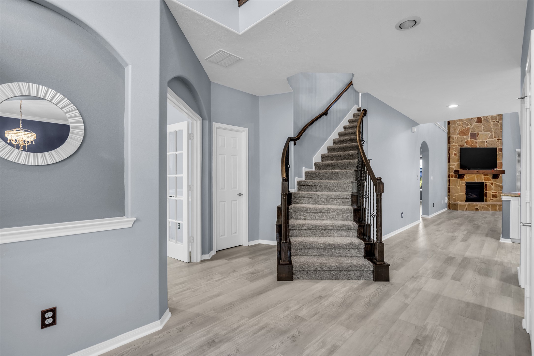 Elegant entryway featuring a graceful curved staircase, modern gray flooring, and a cozy stone fireplace in the living area.