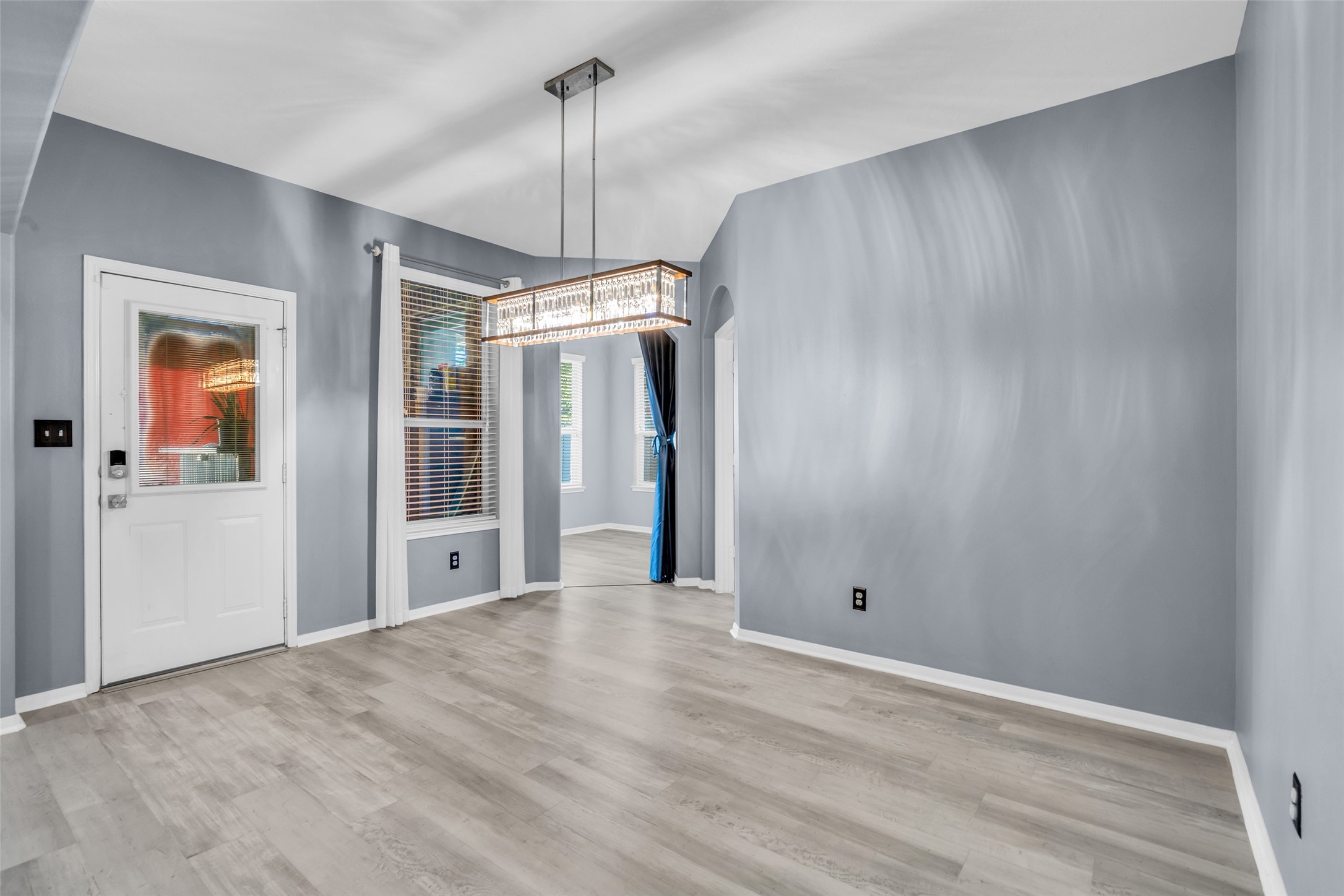 Elegant breakfast area with sleek laminate flooring, modern chandelier, and abundant natural light through large windows.