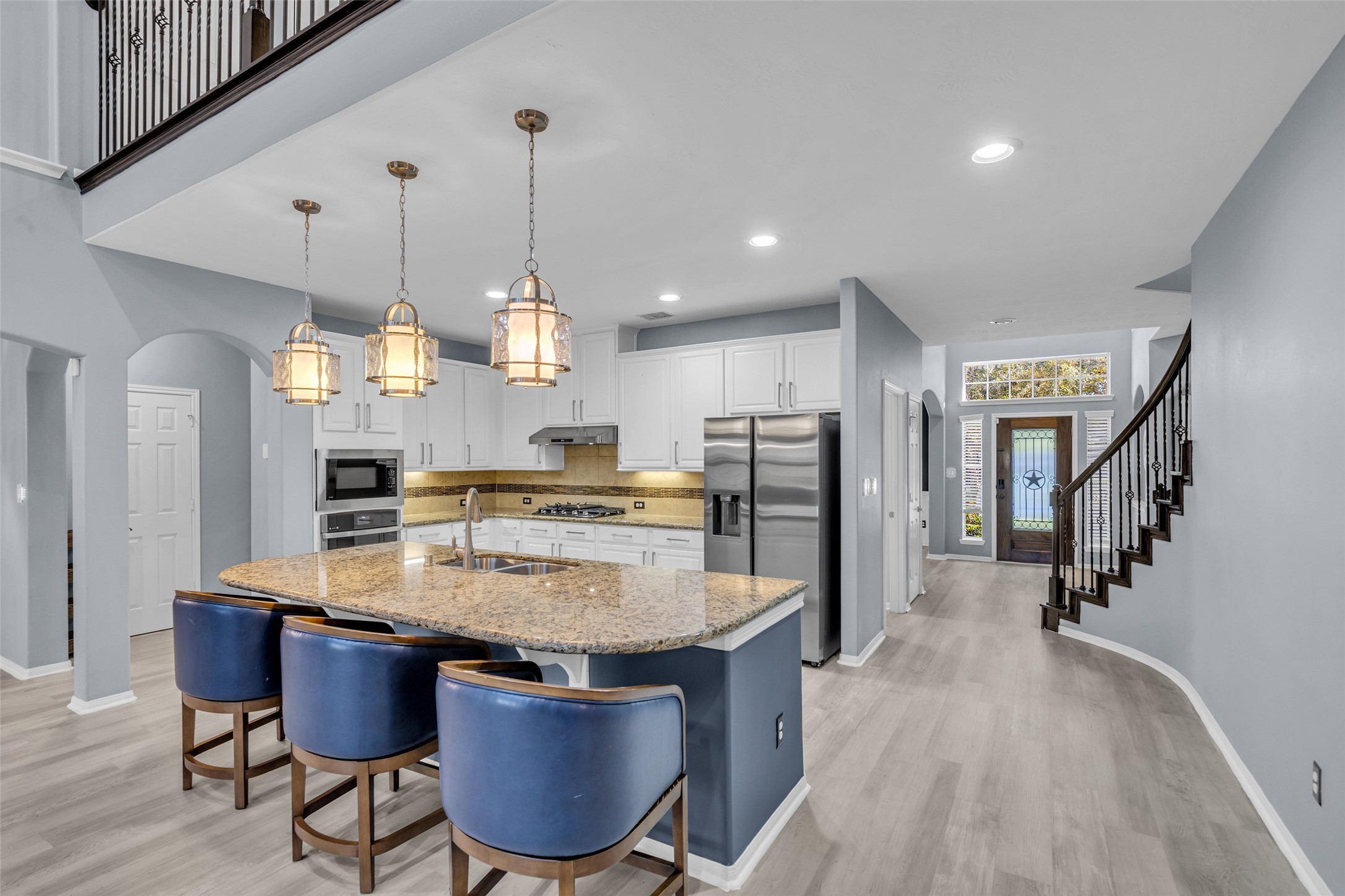 Elegant kitchen with a spacious granite island, modern stainless steel appliances, and stylish pendant lighting, seamlessly connecting to an inviting entryway and curved staircase.