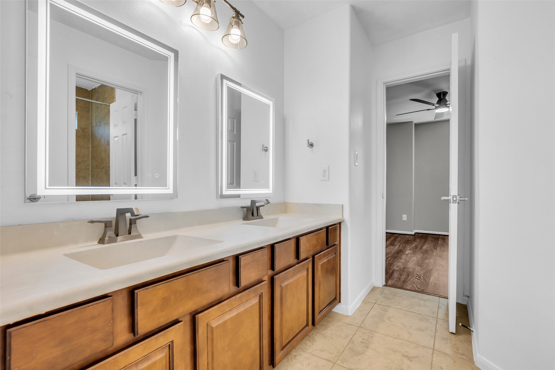 Upstairs secondary jack and jill bathroom featuring a double vanity with illuminated mirrors and stylish fixtures, complemented by warm wood cabinetry and sleek tiling.